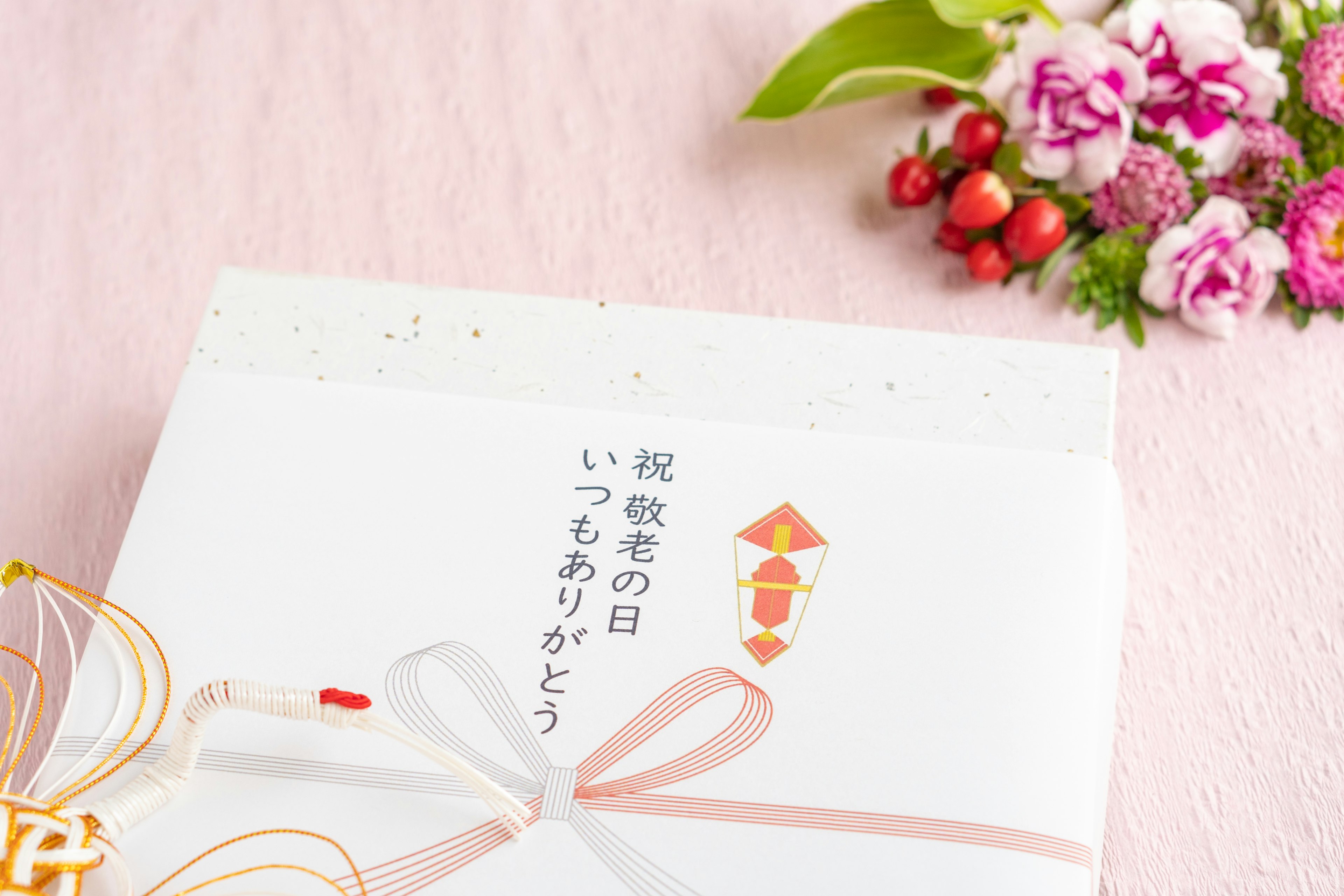 A white envelope tied with a pink ribbon featuring Japanese text and surrounded by flowers