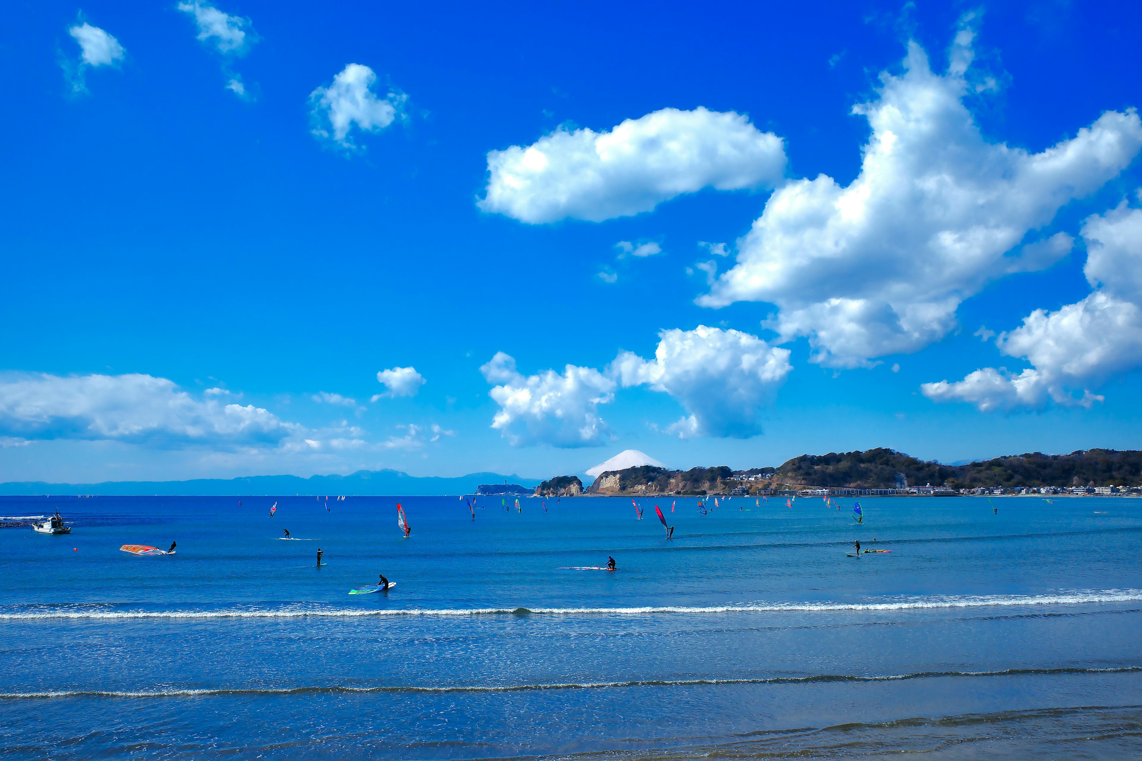 Scenic beach view with blue ocean and sky featuring surfers and boats