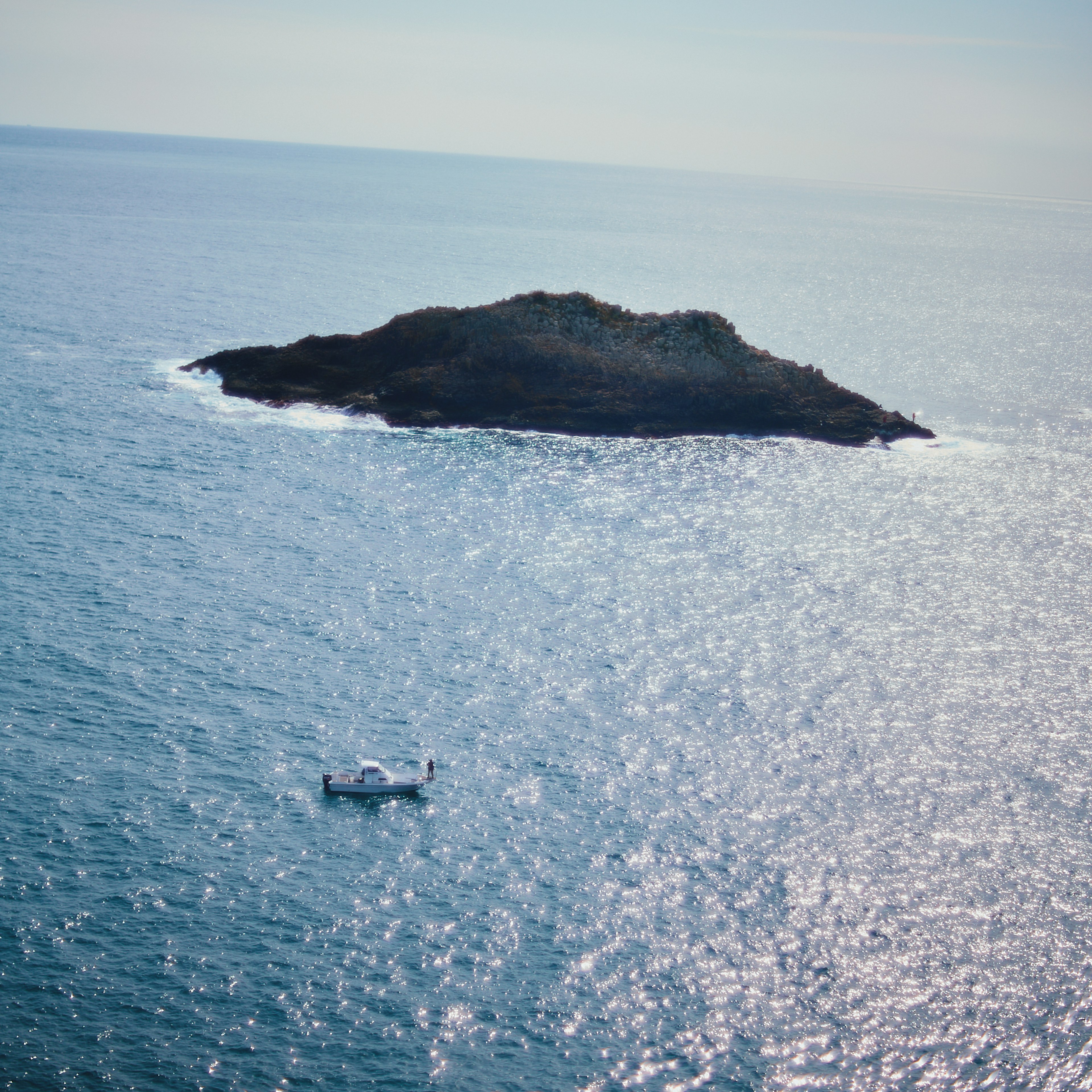 A small island surrounded by blue ocean with a boat nearby