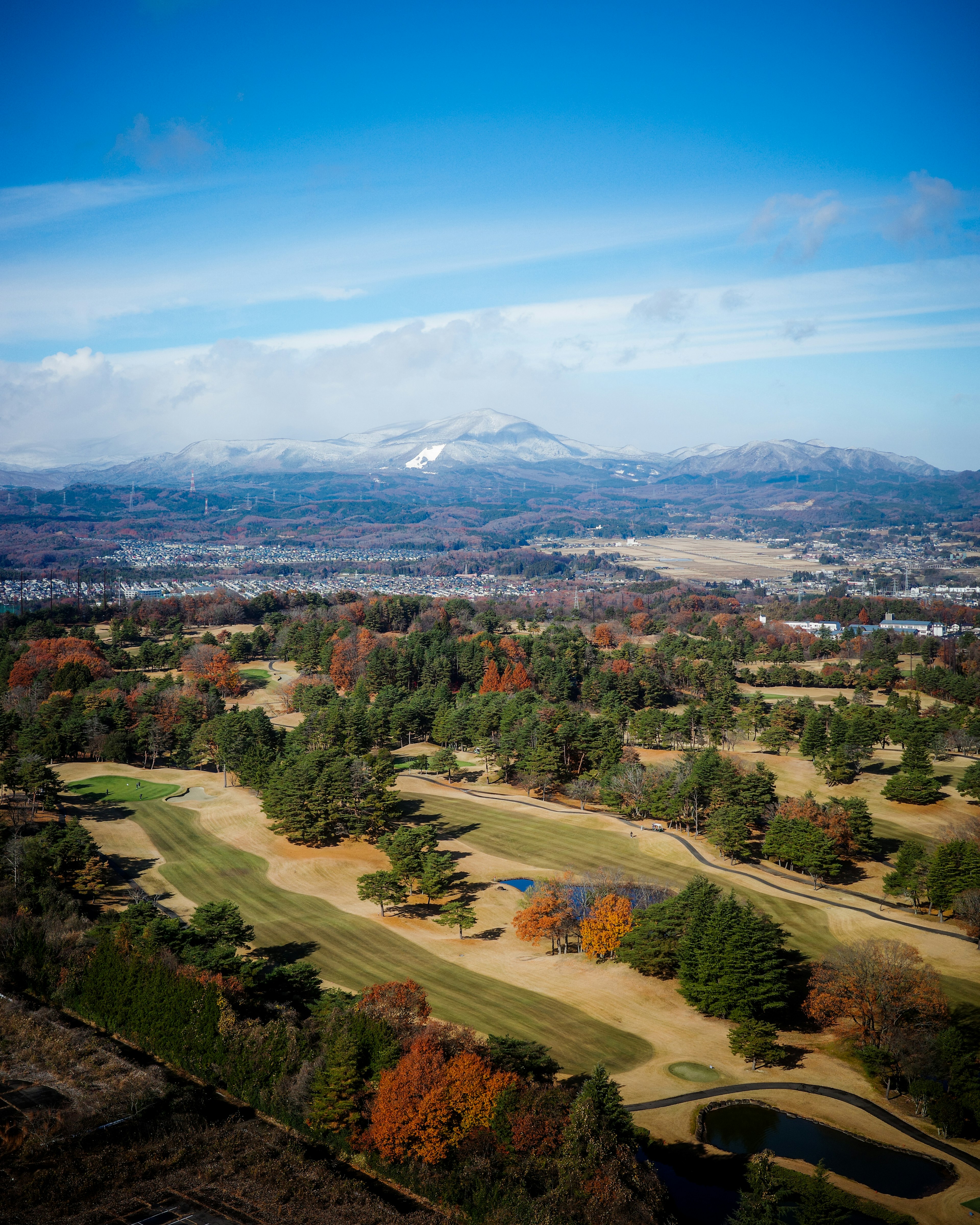 Aerial view of a golf course showcasing vibrant autumn foliage and snow-capped mountains