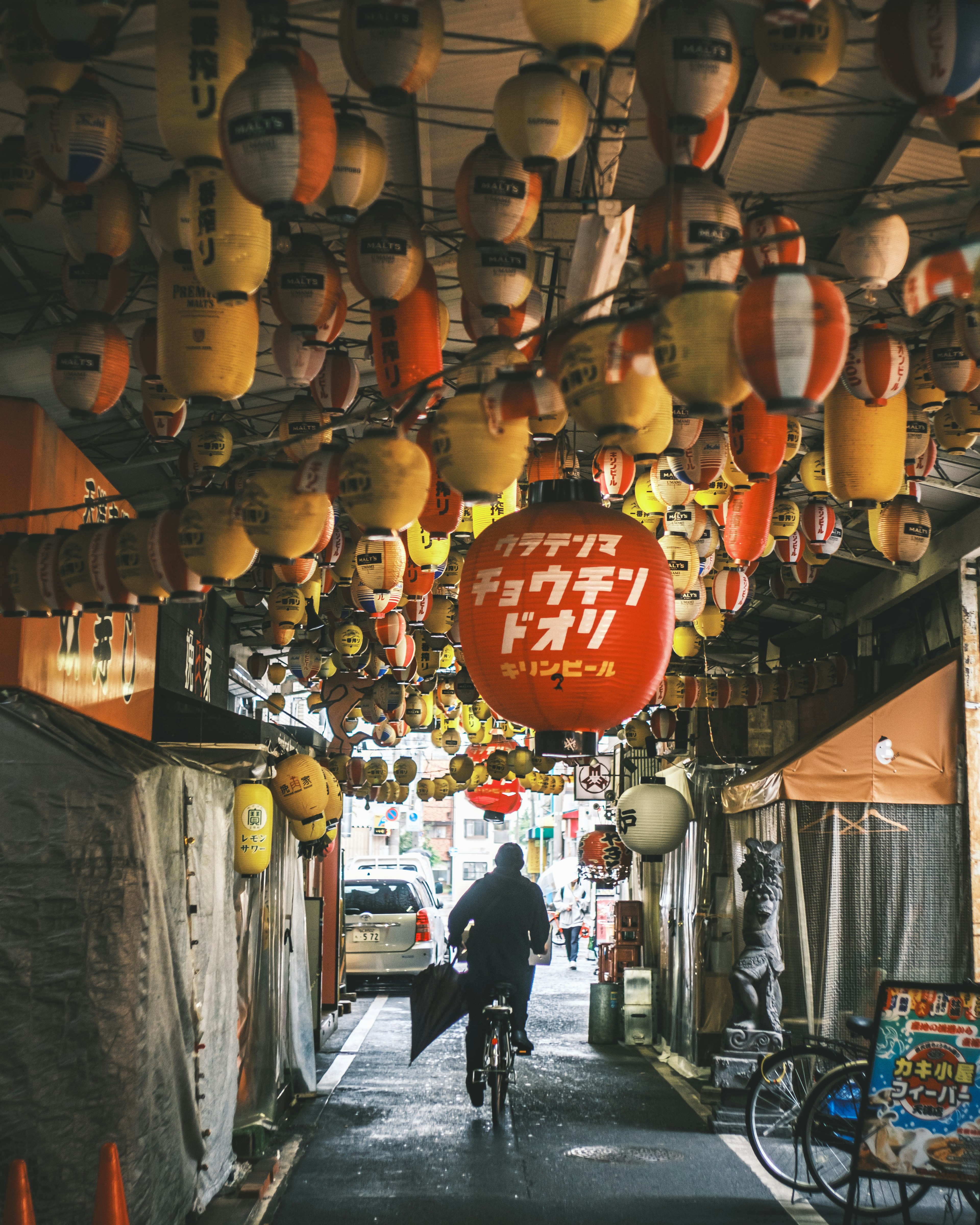 A person riding a bicycle down a narrow street adorned with colorful lanterns