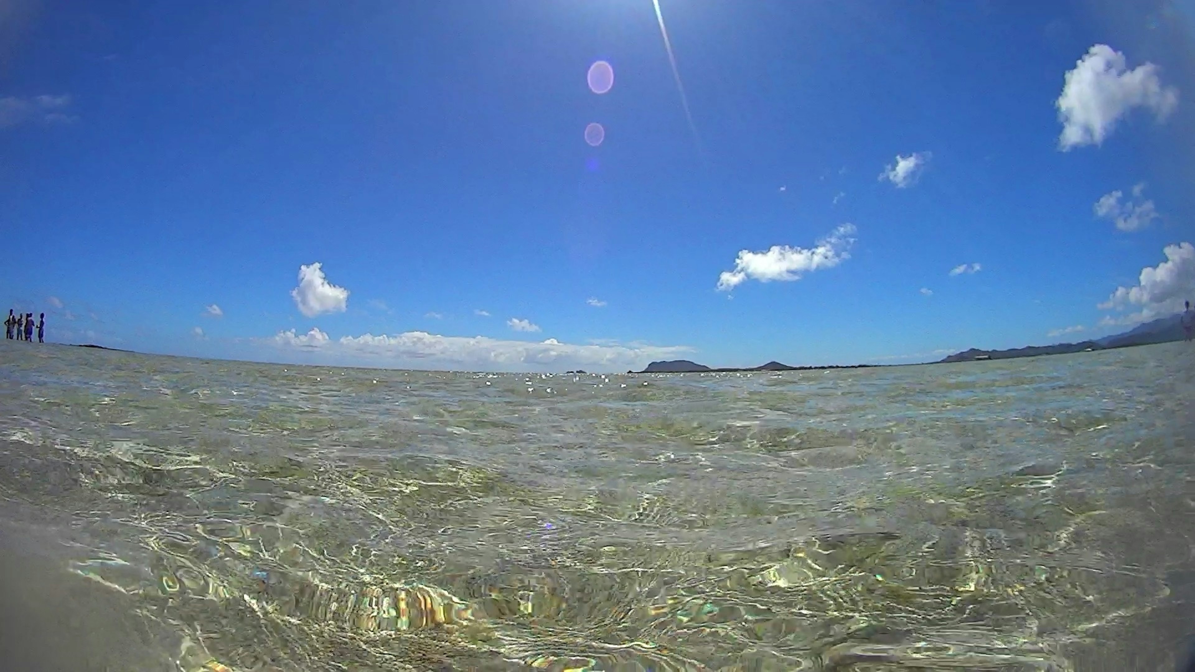 Scenic view of clear ocean water under a blue sky Sunlight reflecting on the water with distant islands