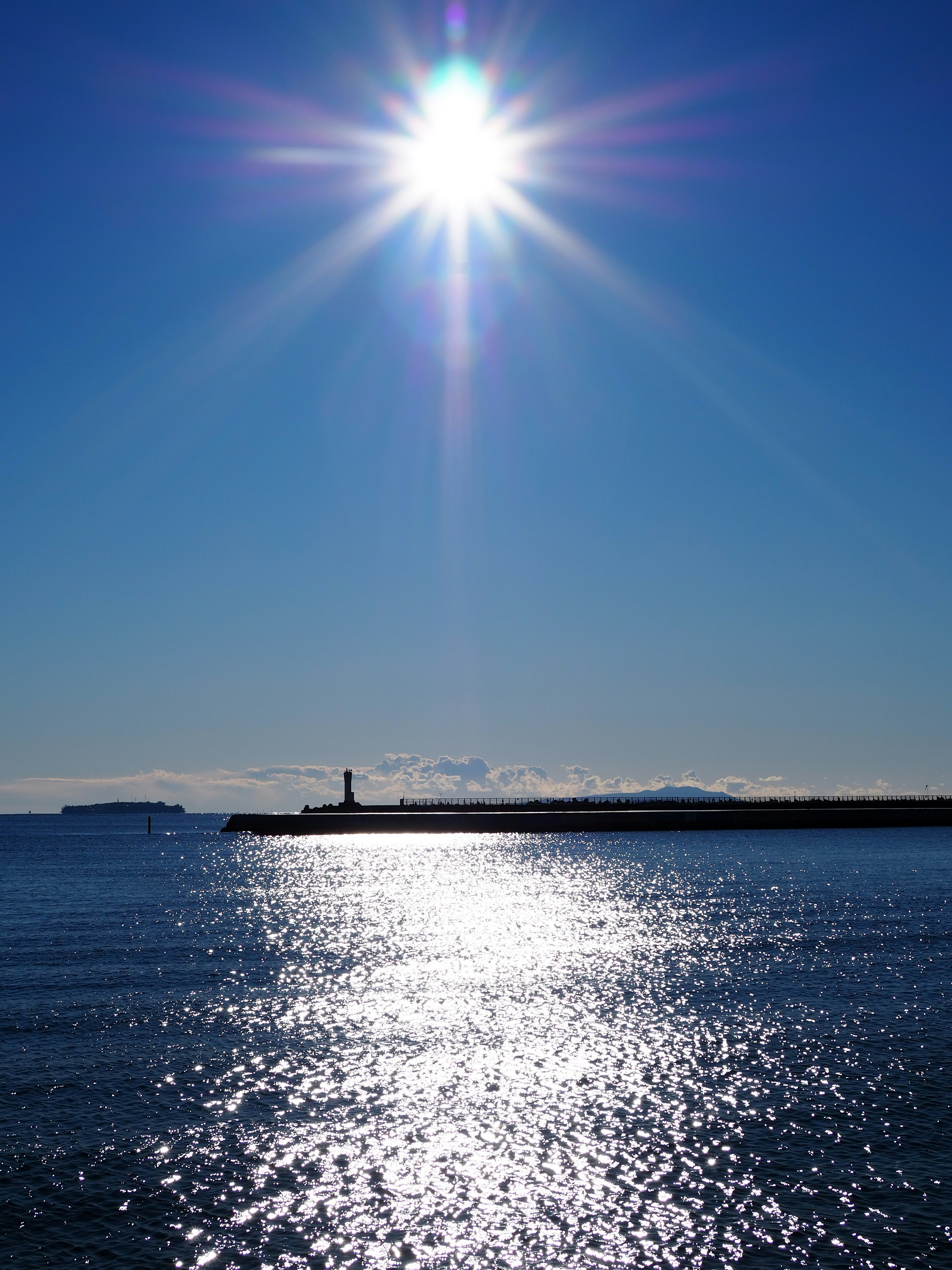 Bright sun shining over calm sea with lighthouse silhouette