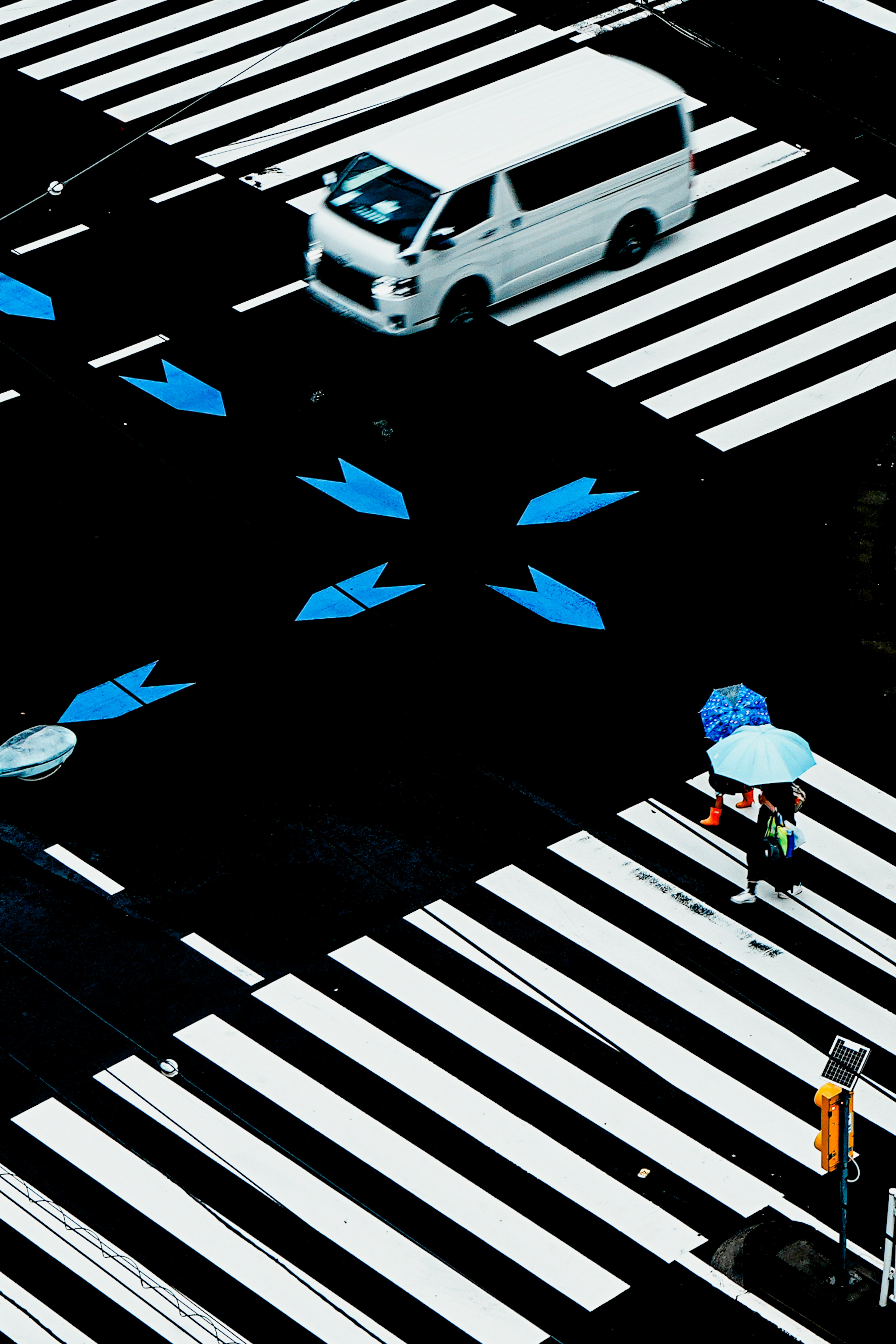 Sebuah kendaraan putih di zebra cross dengan panah biru dan seseorang yang memegang payung