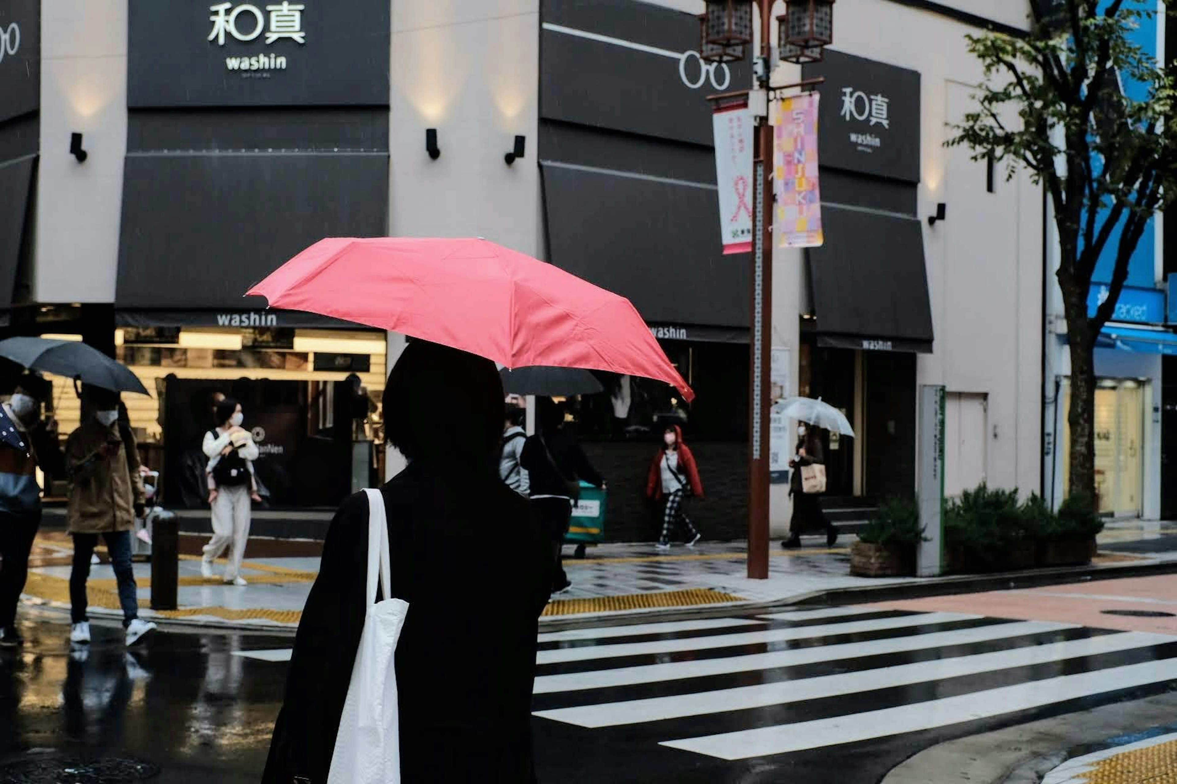 雨の中、ピンクの傘を持つ人が横断歩道を渡る風景