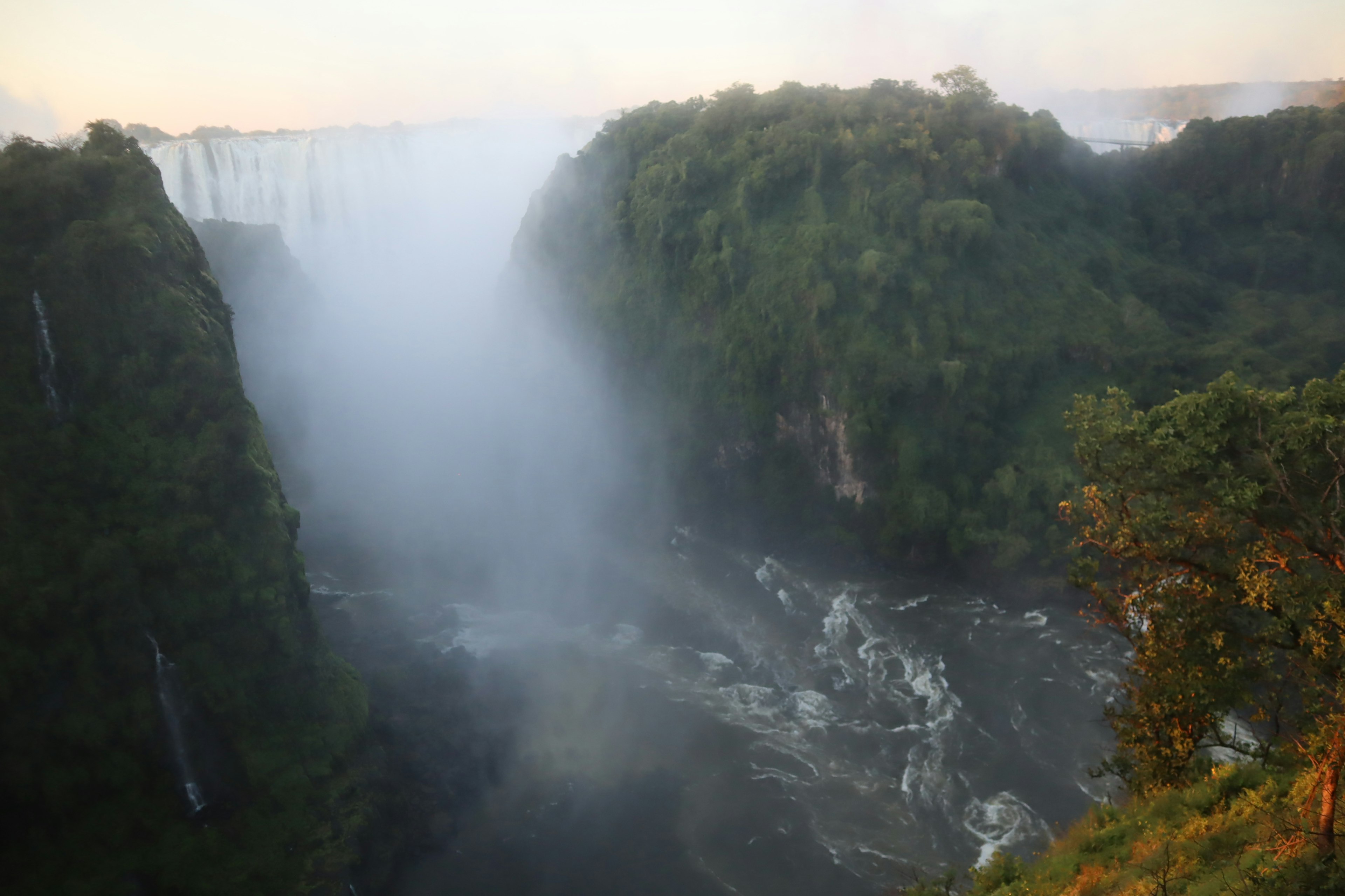 Pemandangan dramatis Air Terjun Iguazu kabut naik di atas air yang mengalir vegetasi hijau yang rimbun di sekitarnya