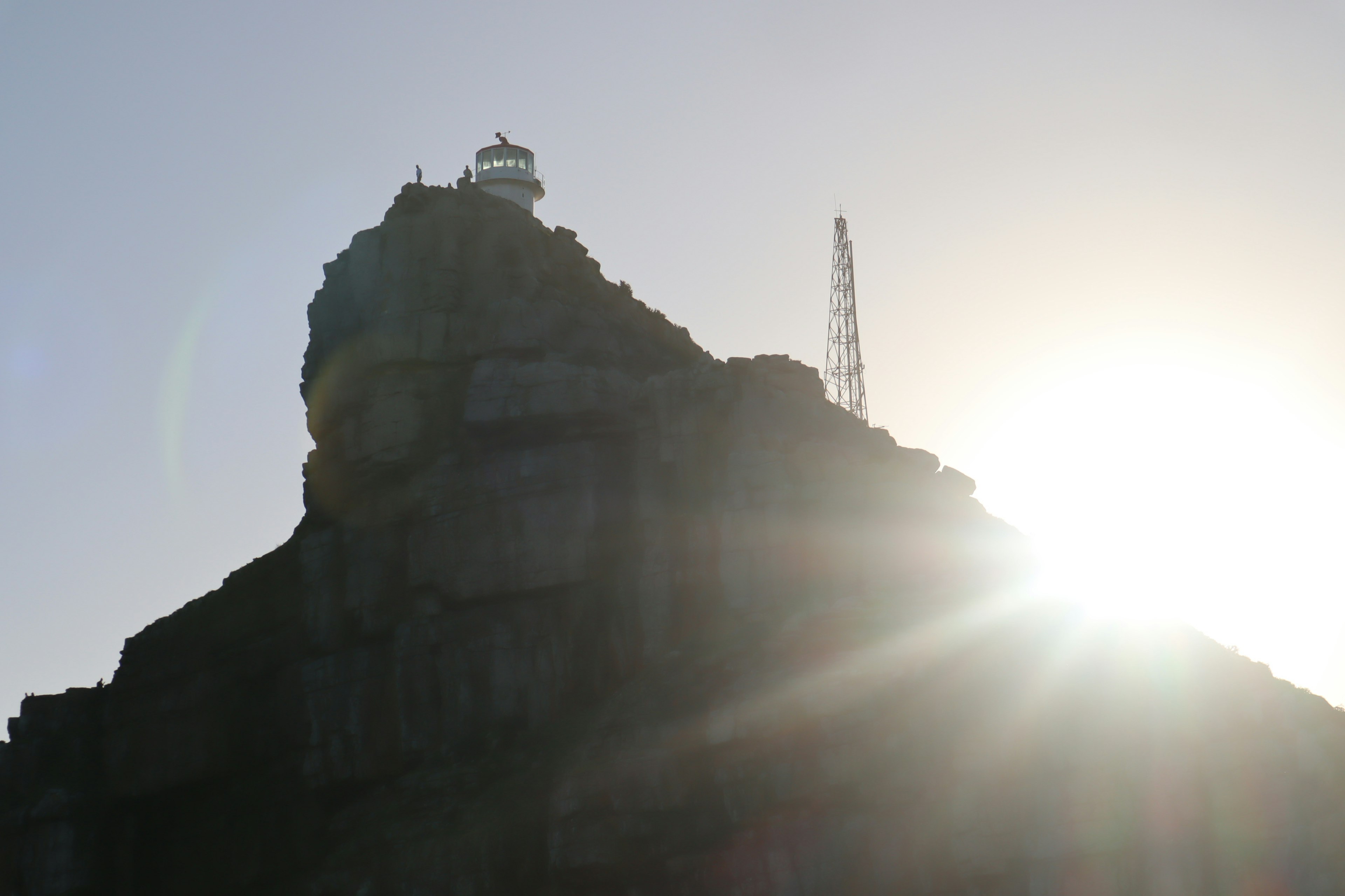 Silhouette d'un phare et d'une tour de communication sur une colline rocheuse au coucher du soleil