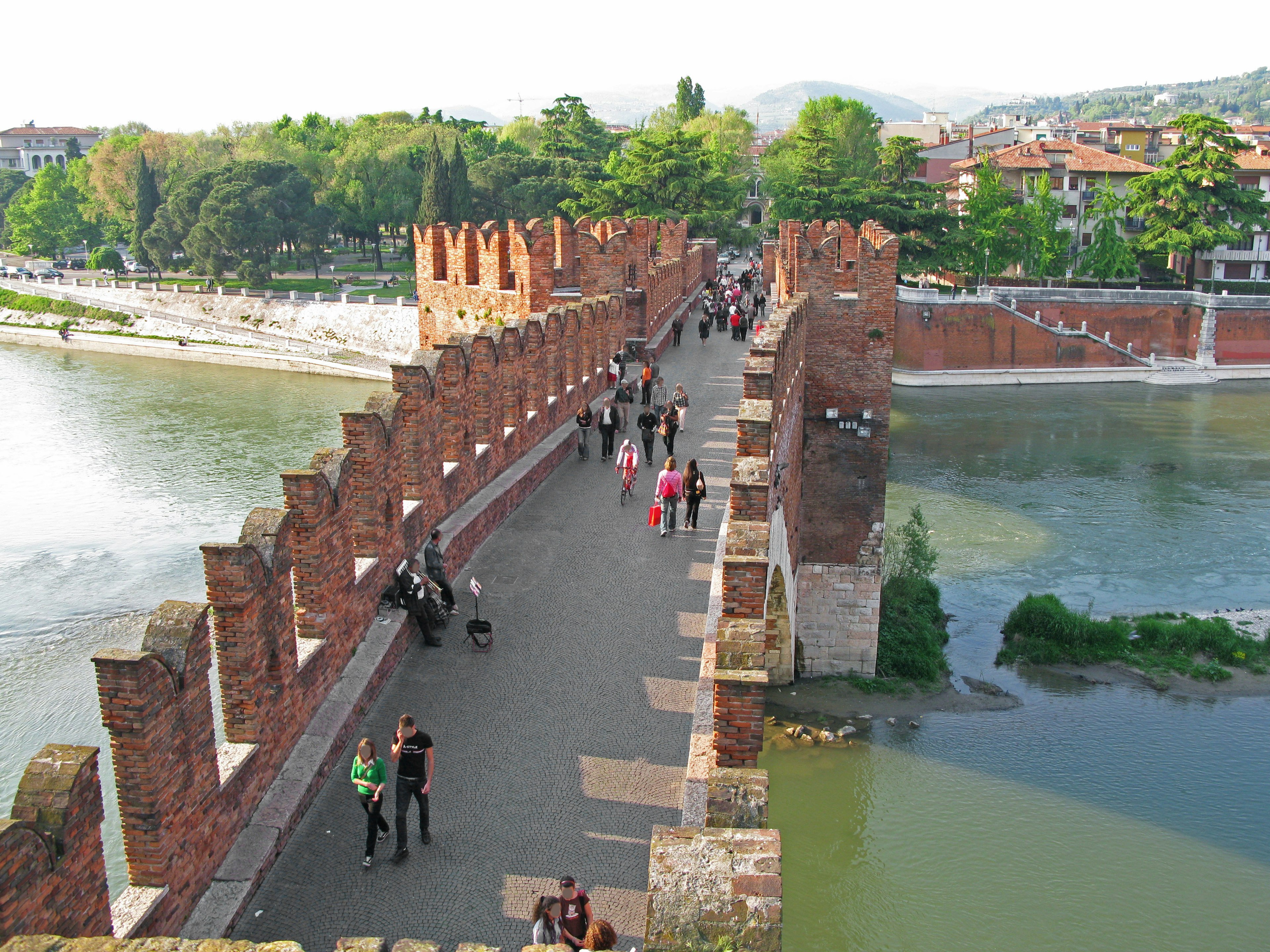 Tourists walking on the scenic Adige River bridge with lush greenery