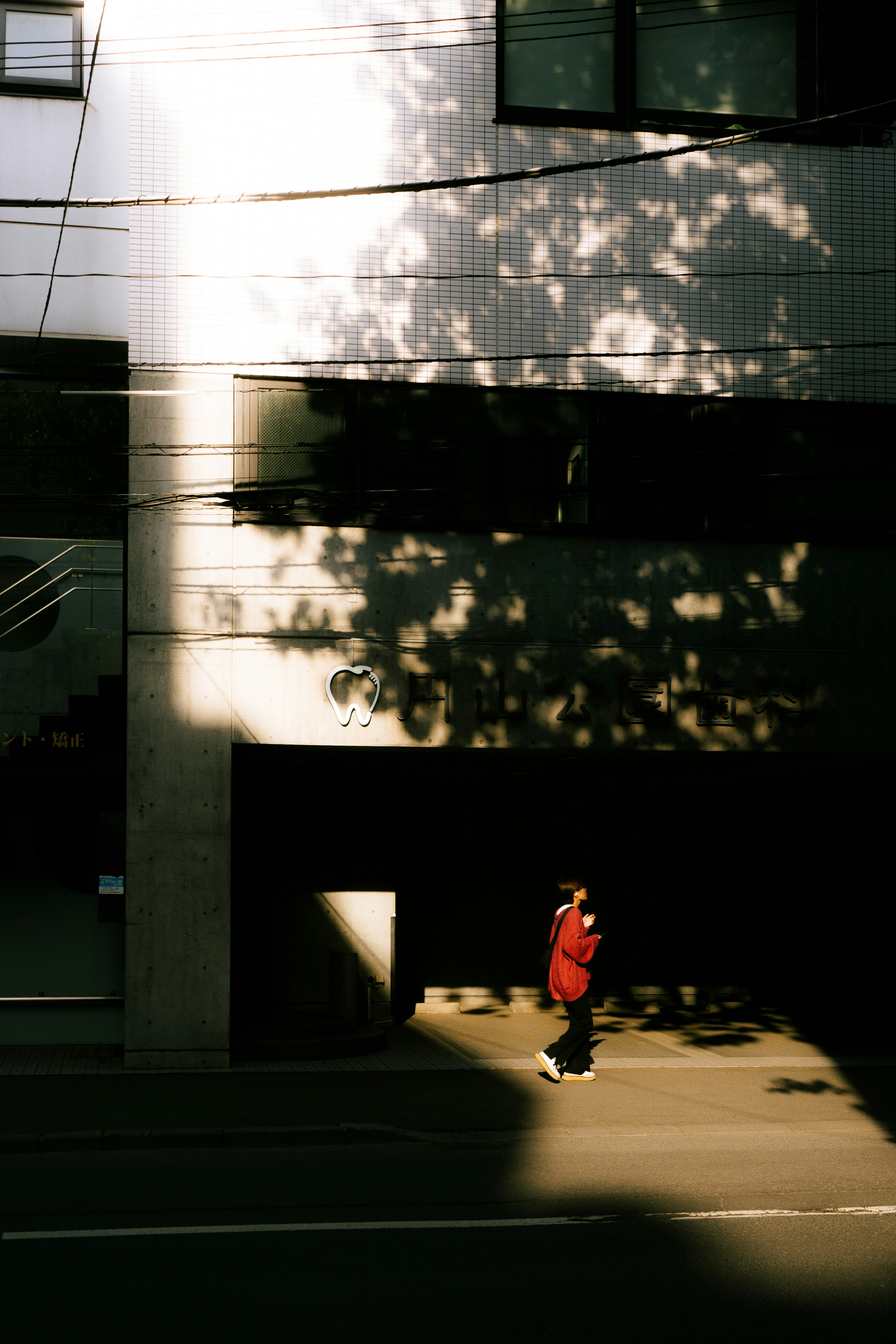 赤い服を着た人物が影のある街路を歩いている