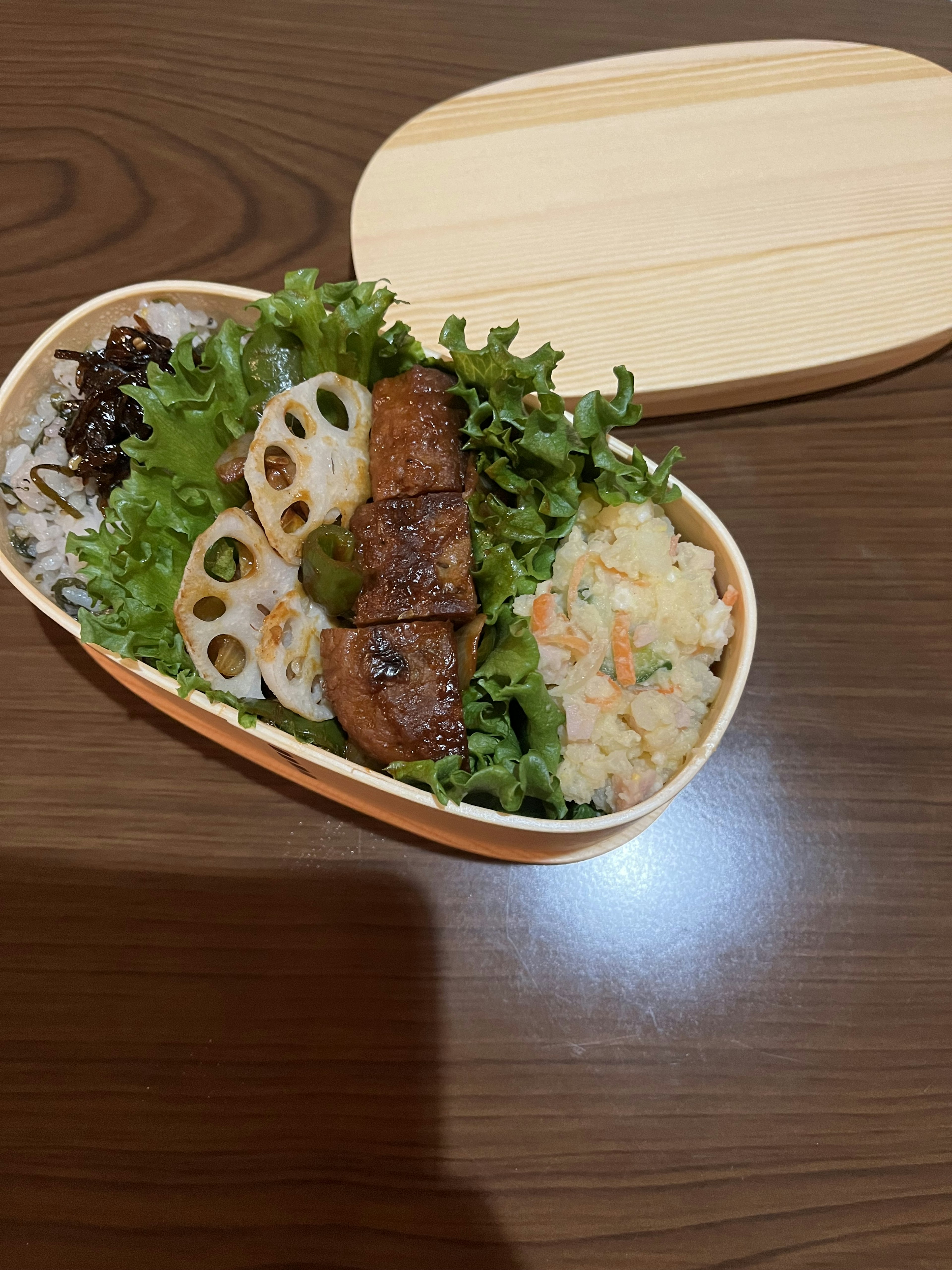 Un bento splendidamente disposto con lattuga, radice di loto e carne