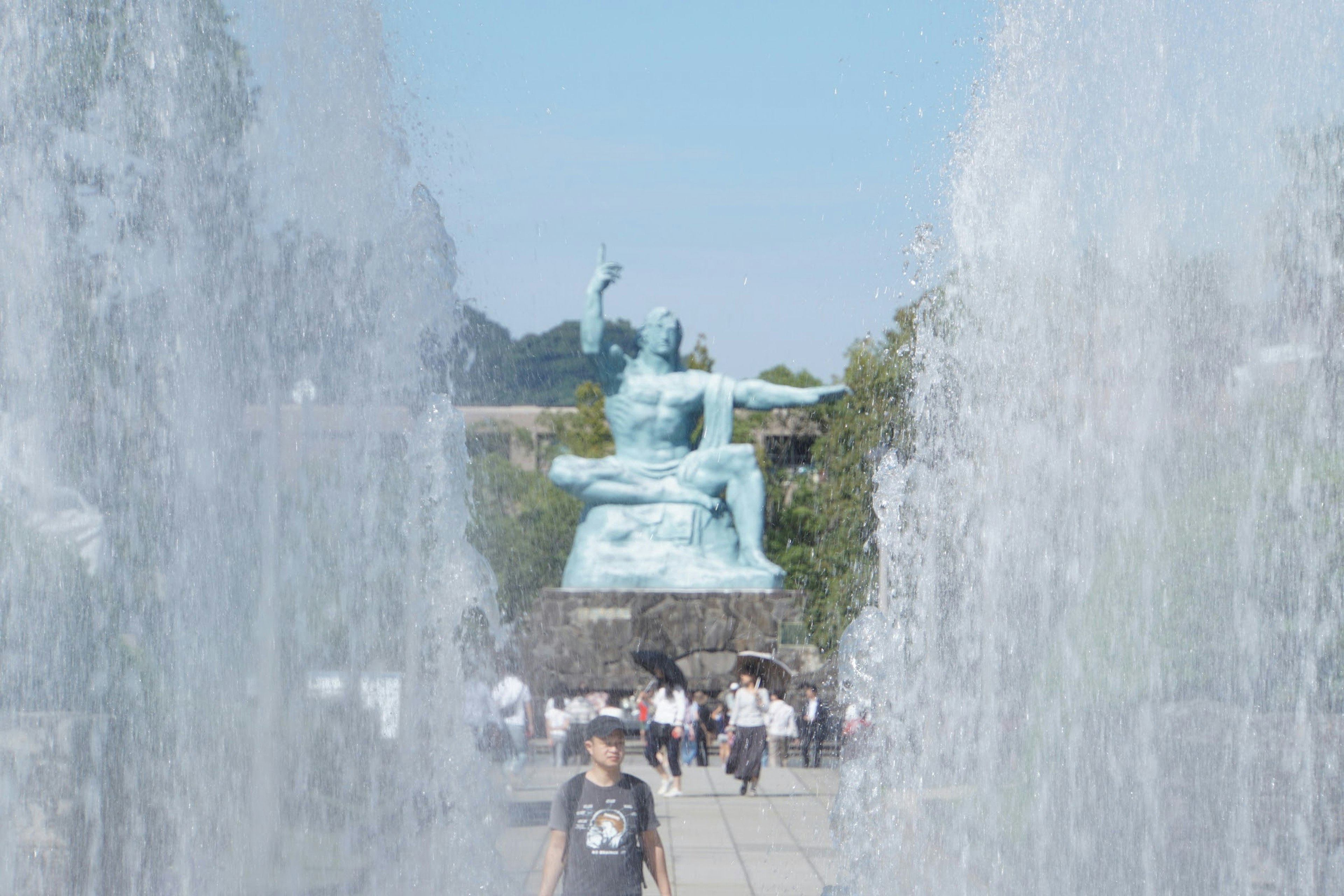 People walking in front of a bronze statue with fountains in the foreground