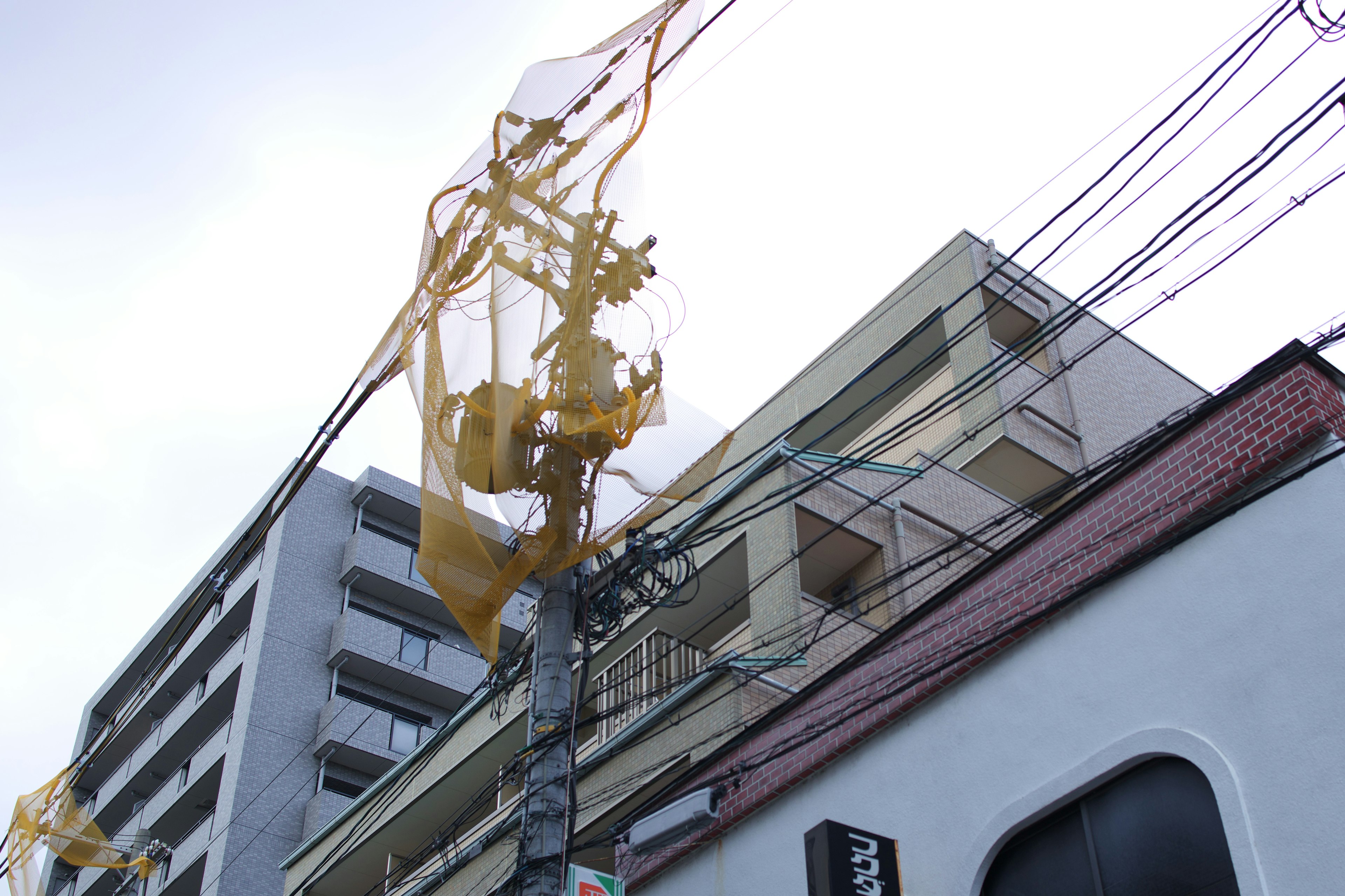 A view of a building with a yellow mesh netting and intersecting power lines