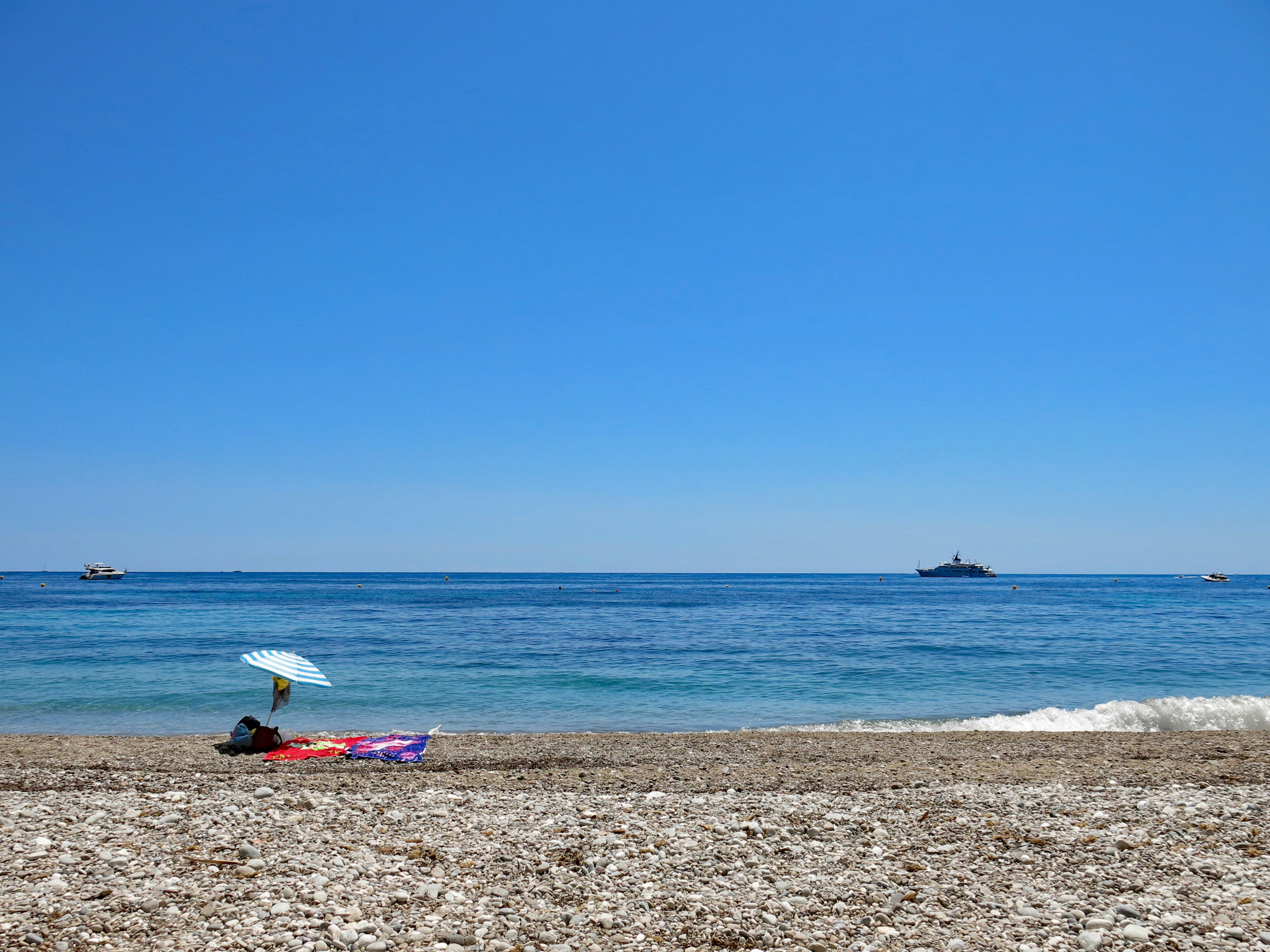 Scène de plage avec ciel bleu clair et mer calme, une personne sous un parasol