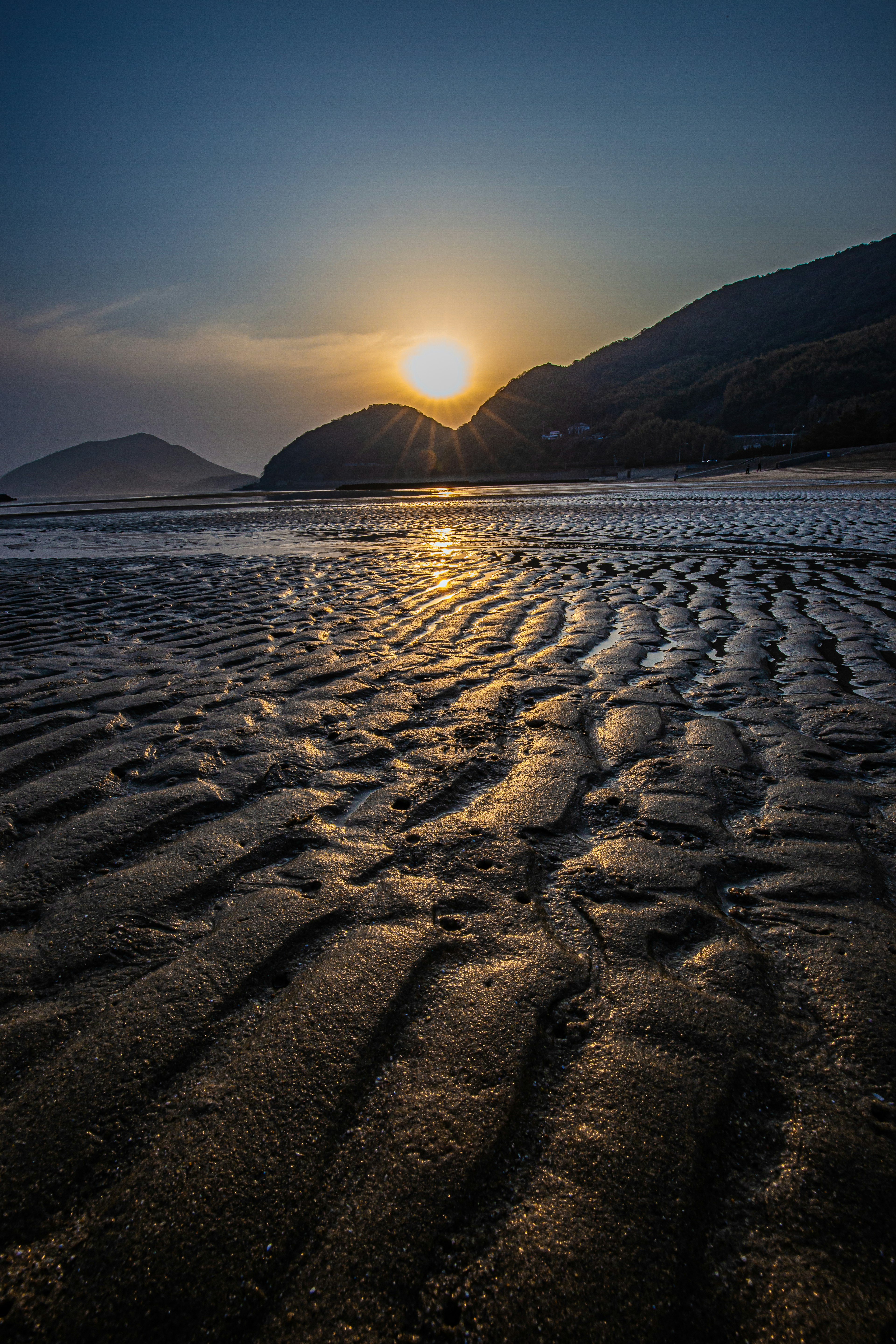 夕日が照らす海岸の砂紋と山のシルエット