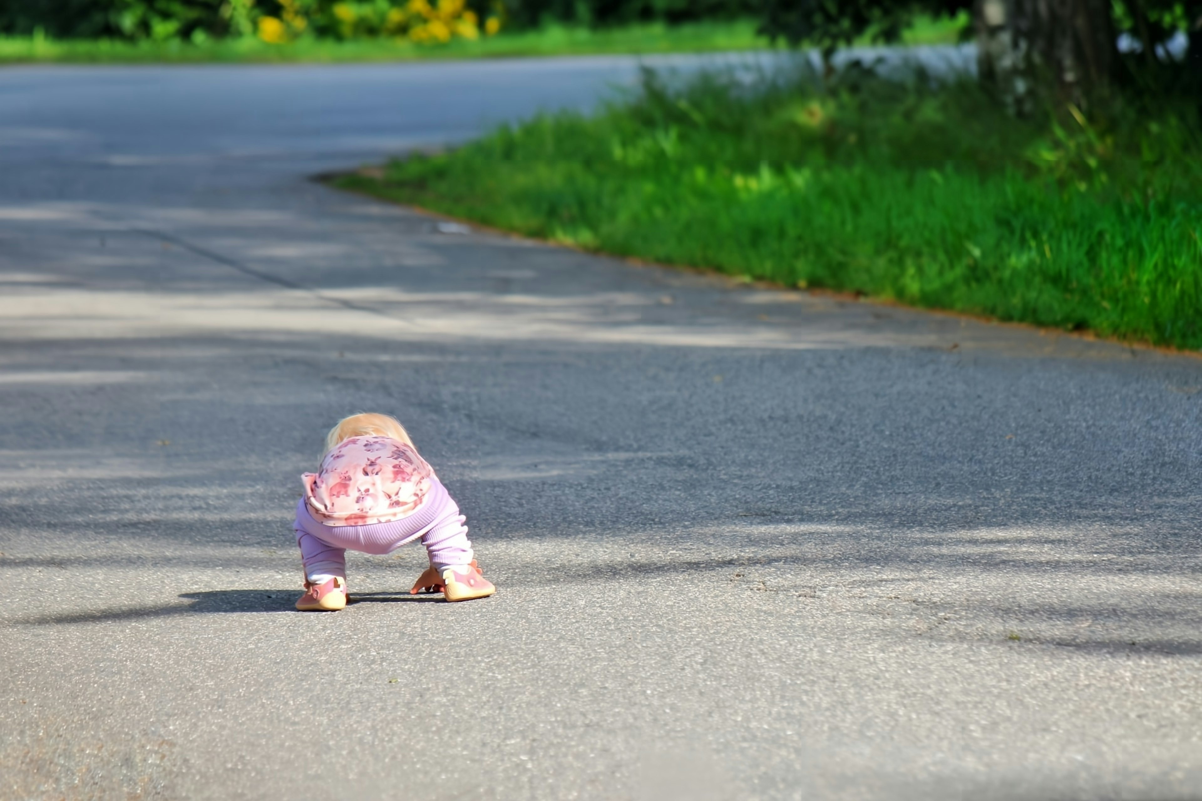 Baby crawling on the road surrounded by grass and trees