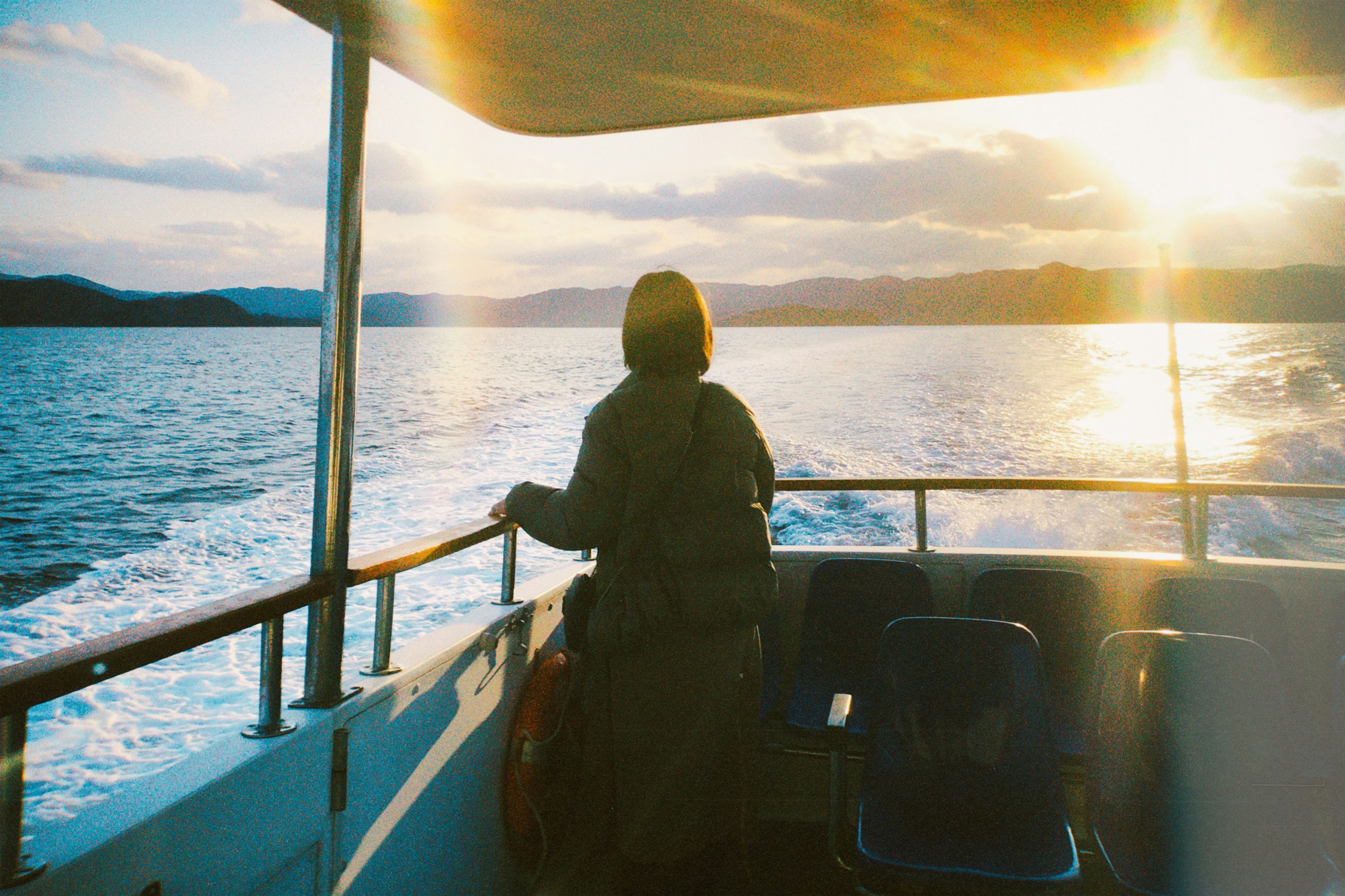 Une personne se tenant sur un bateau regardant la mer avec le coucher de soleil en arrière-plan