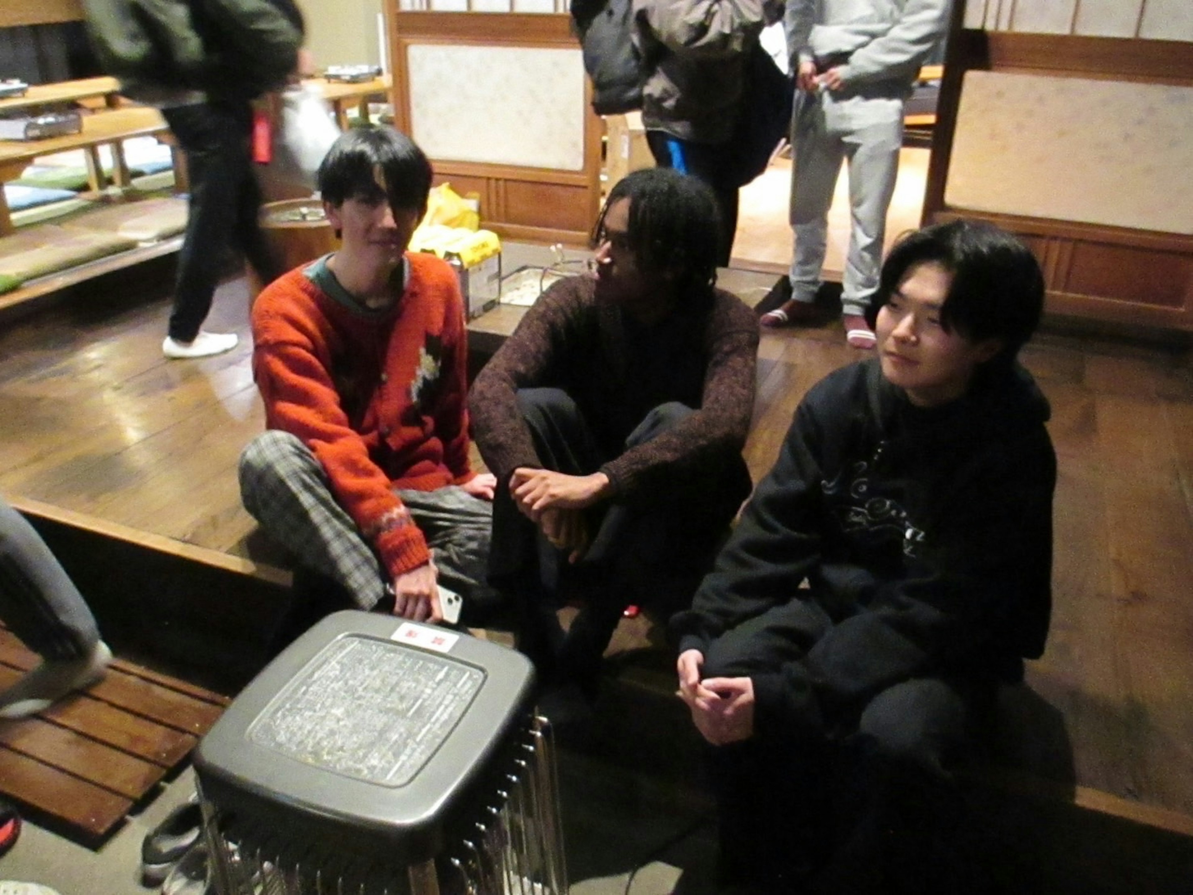 Three young people sitting indoors near a heating device