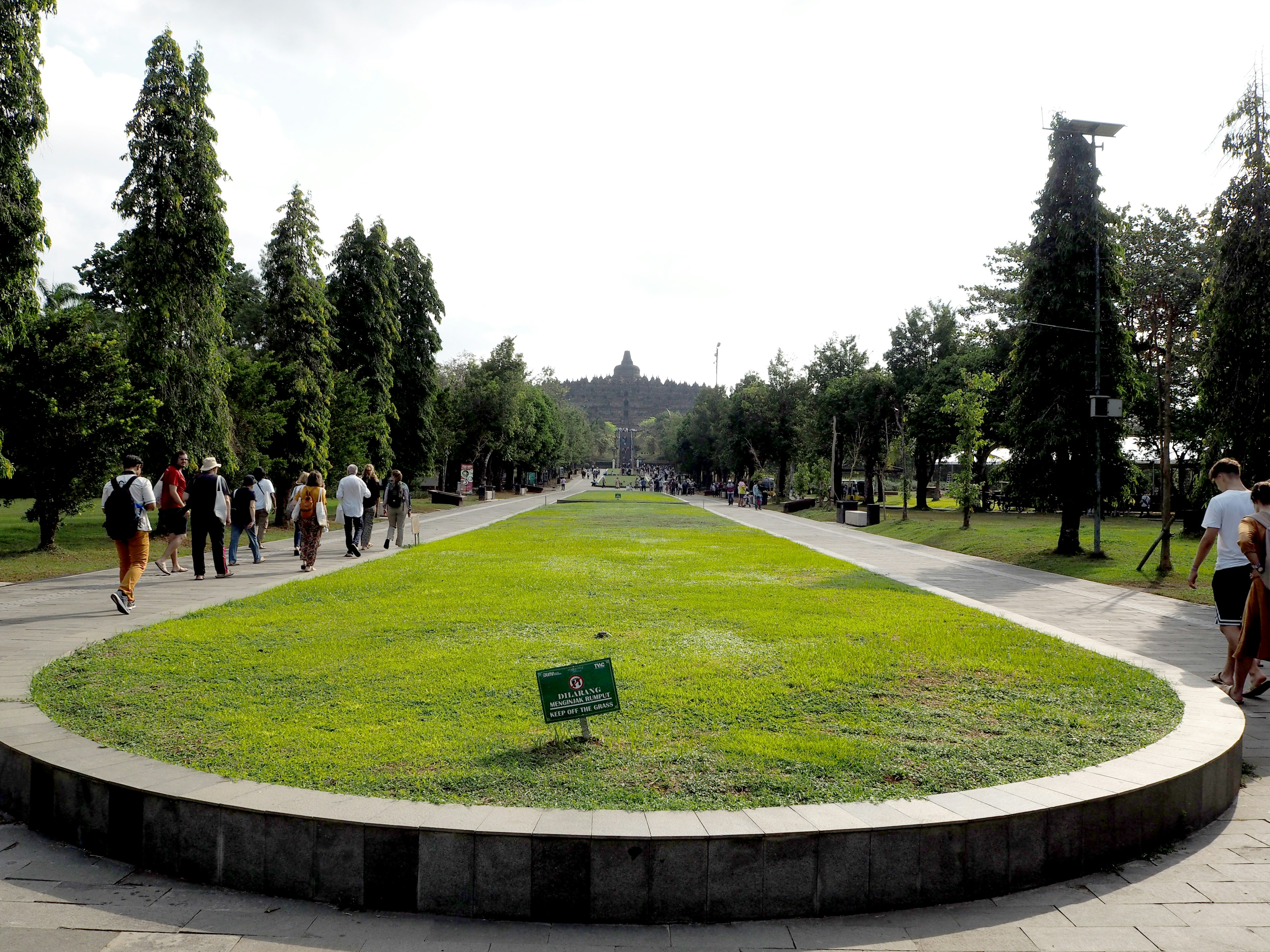 人們在綠意盎然的公園小徑上散步，遠處有一座佛教寺廟