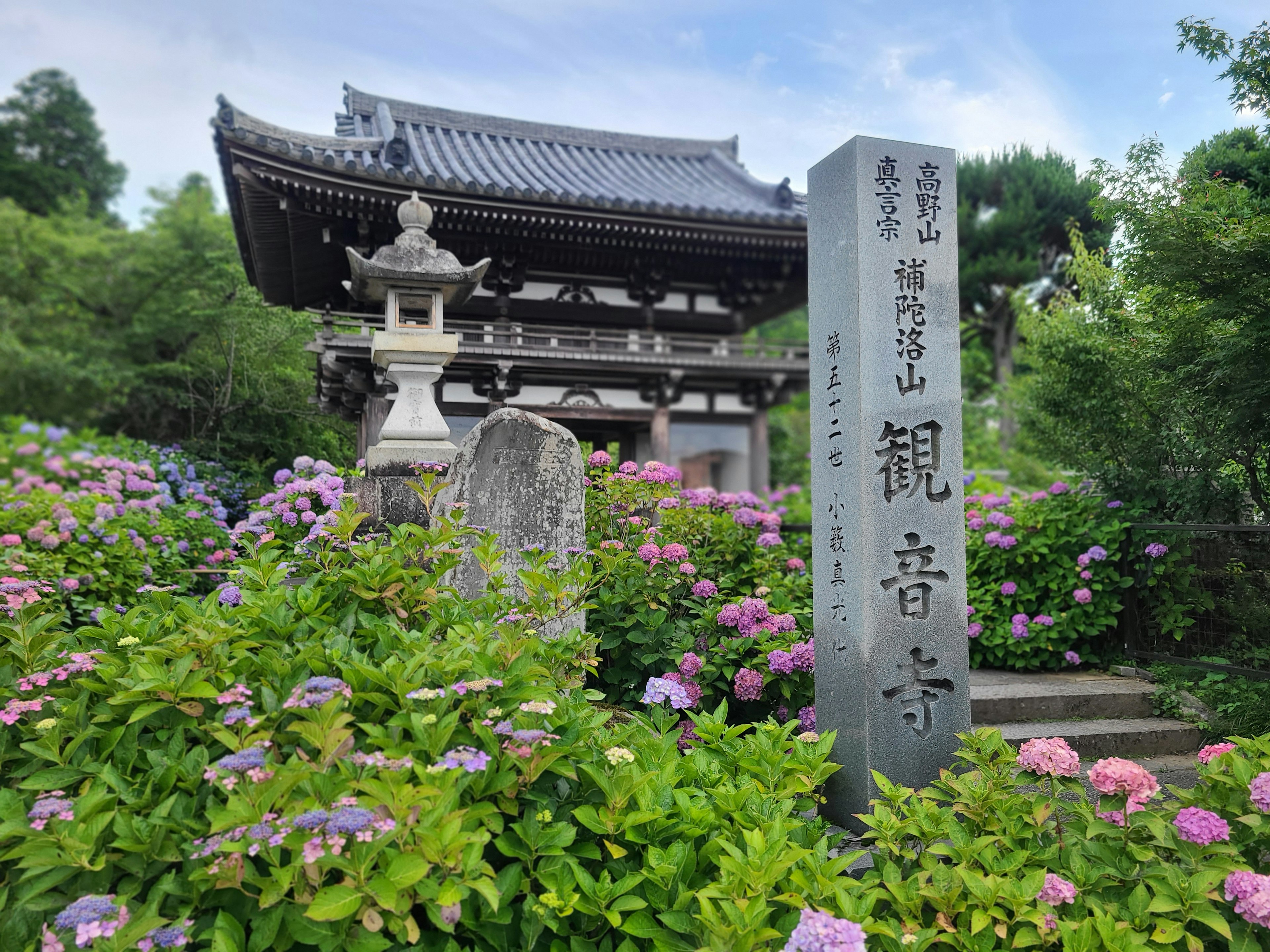 Monumento de piedra del templo Kannonji rodeado de flores y arquitectura tradicional