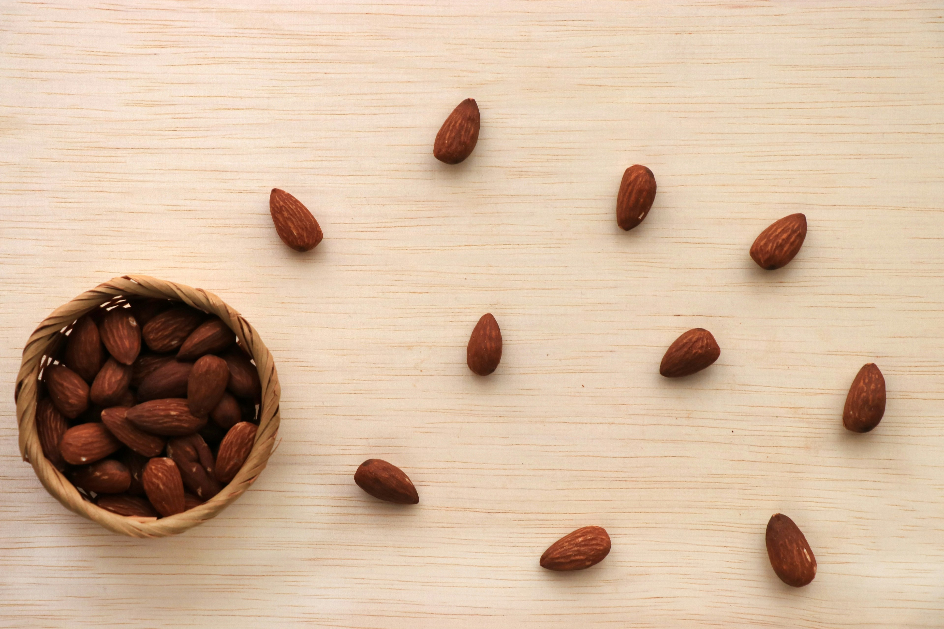 Almonds scattered on a wooden surface with a small bowl filled with almonds