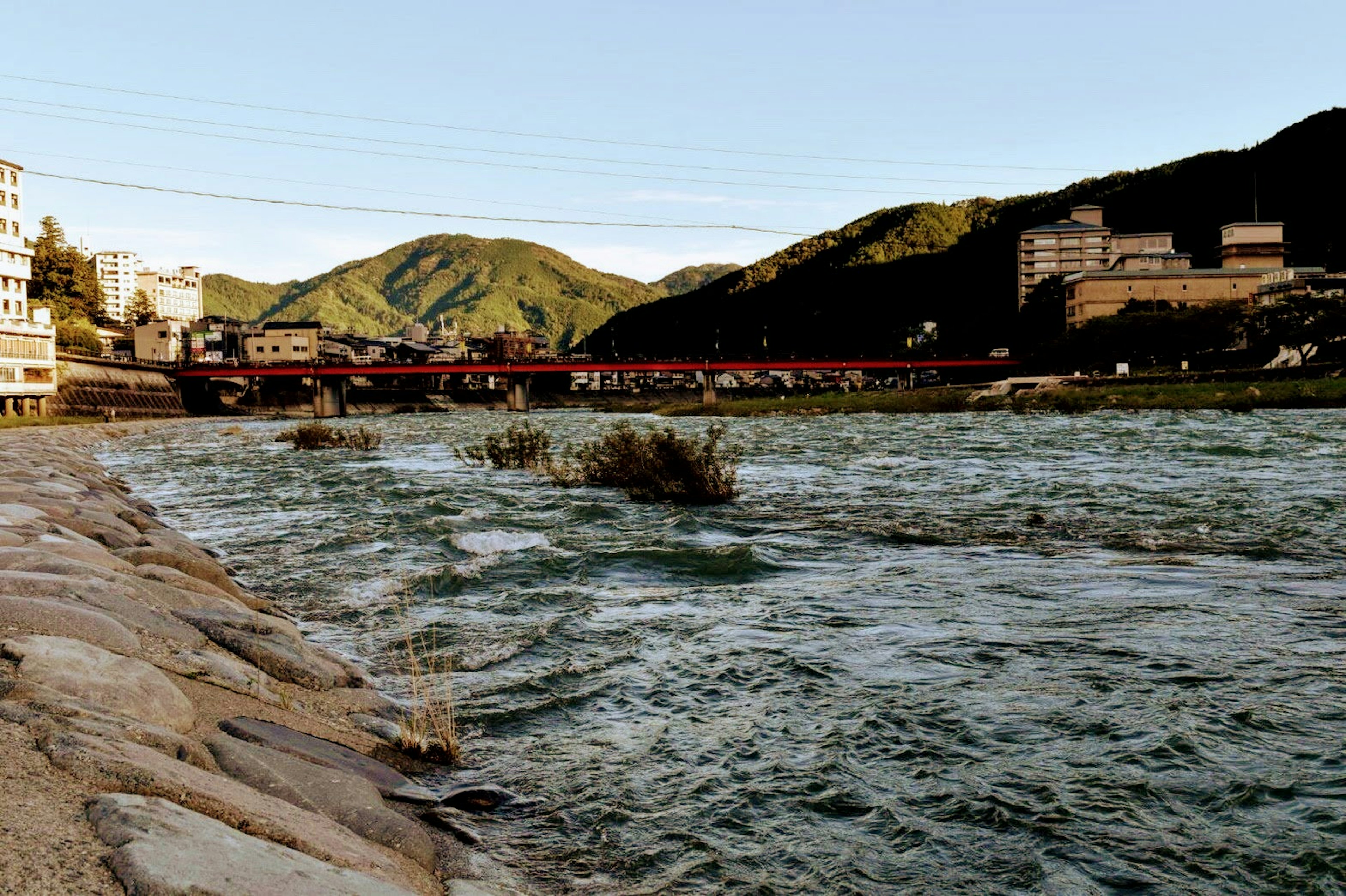 Vista escénica del río con montañas y edificios visibles que mezclan naturaleza y elementos urbanos