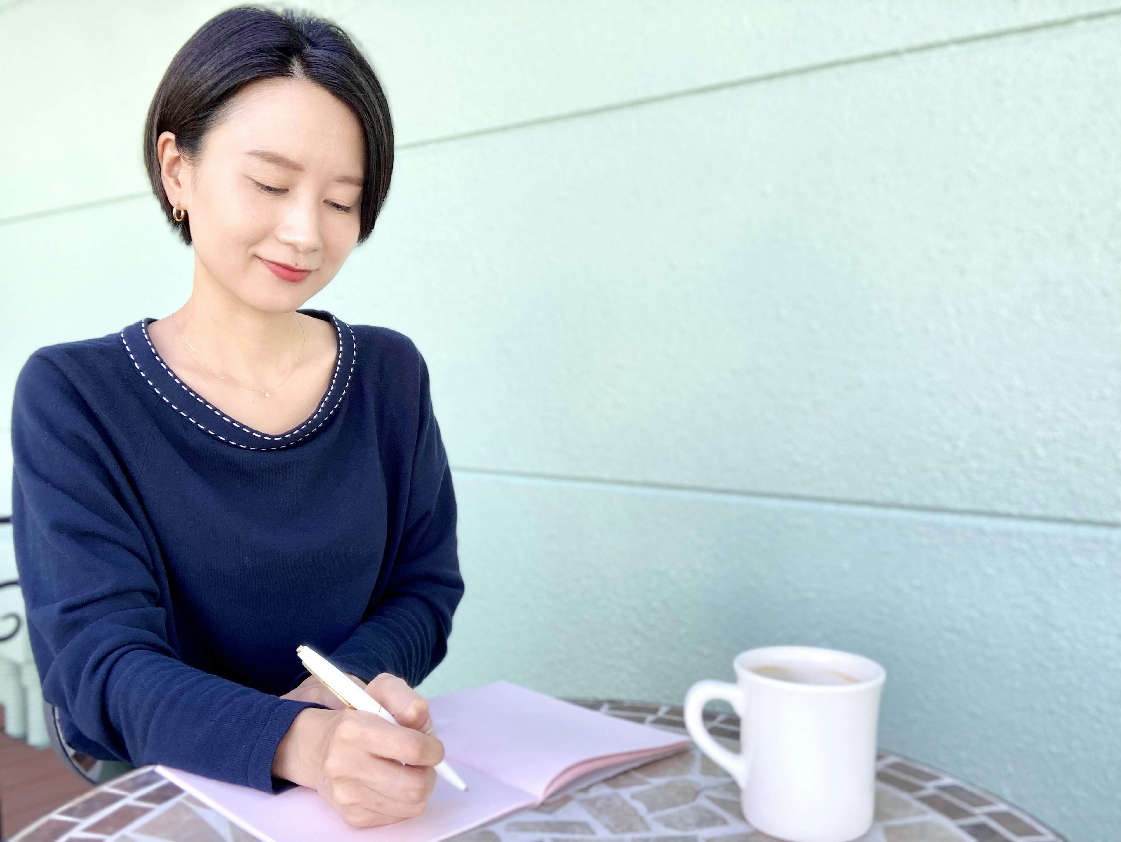 A woman writing in a notebook at a cafe table with a coffee cup