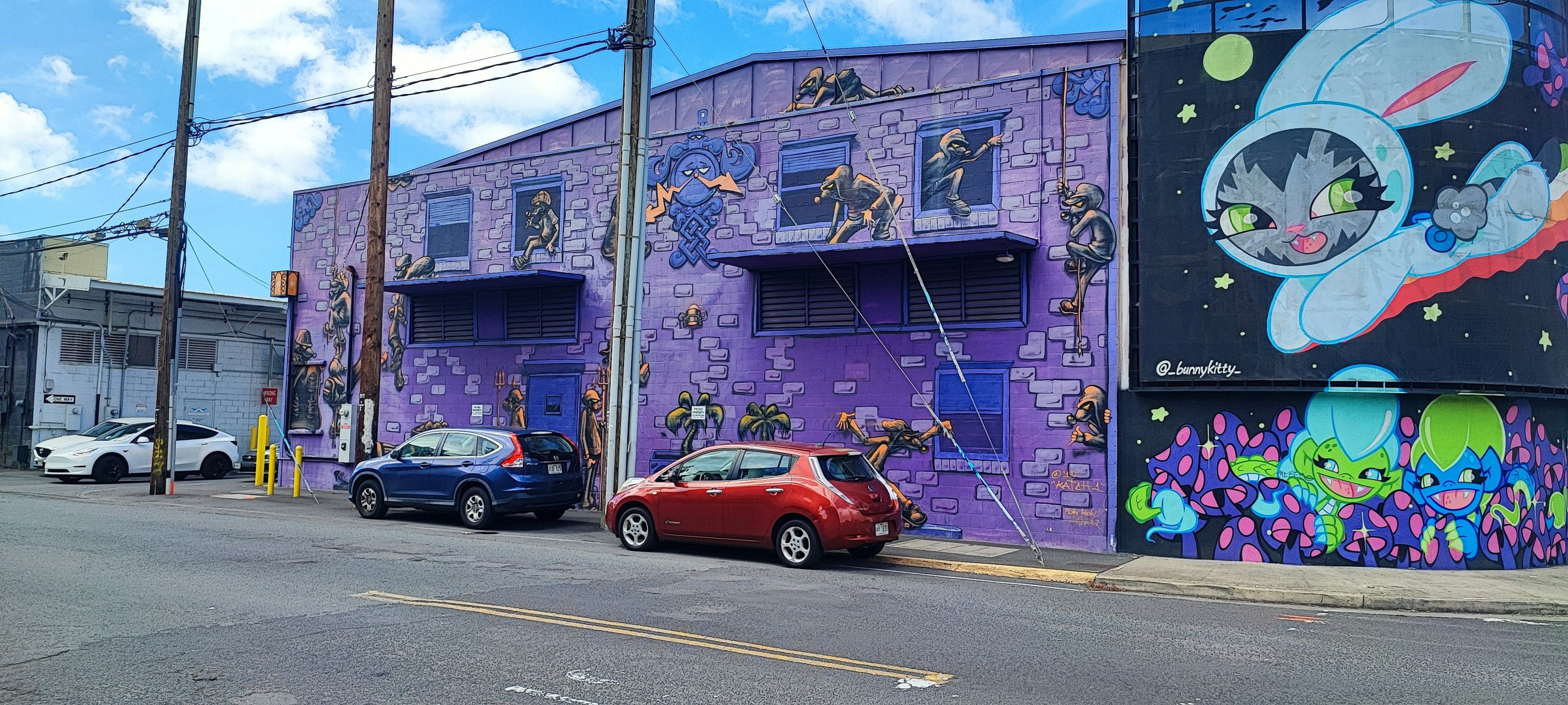 Vue de rue avec un bâtiment violet orné de peintures murales uniques et de voitures garées