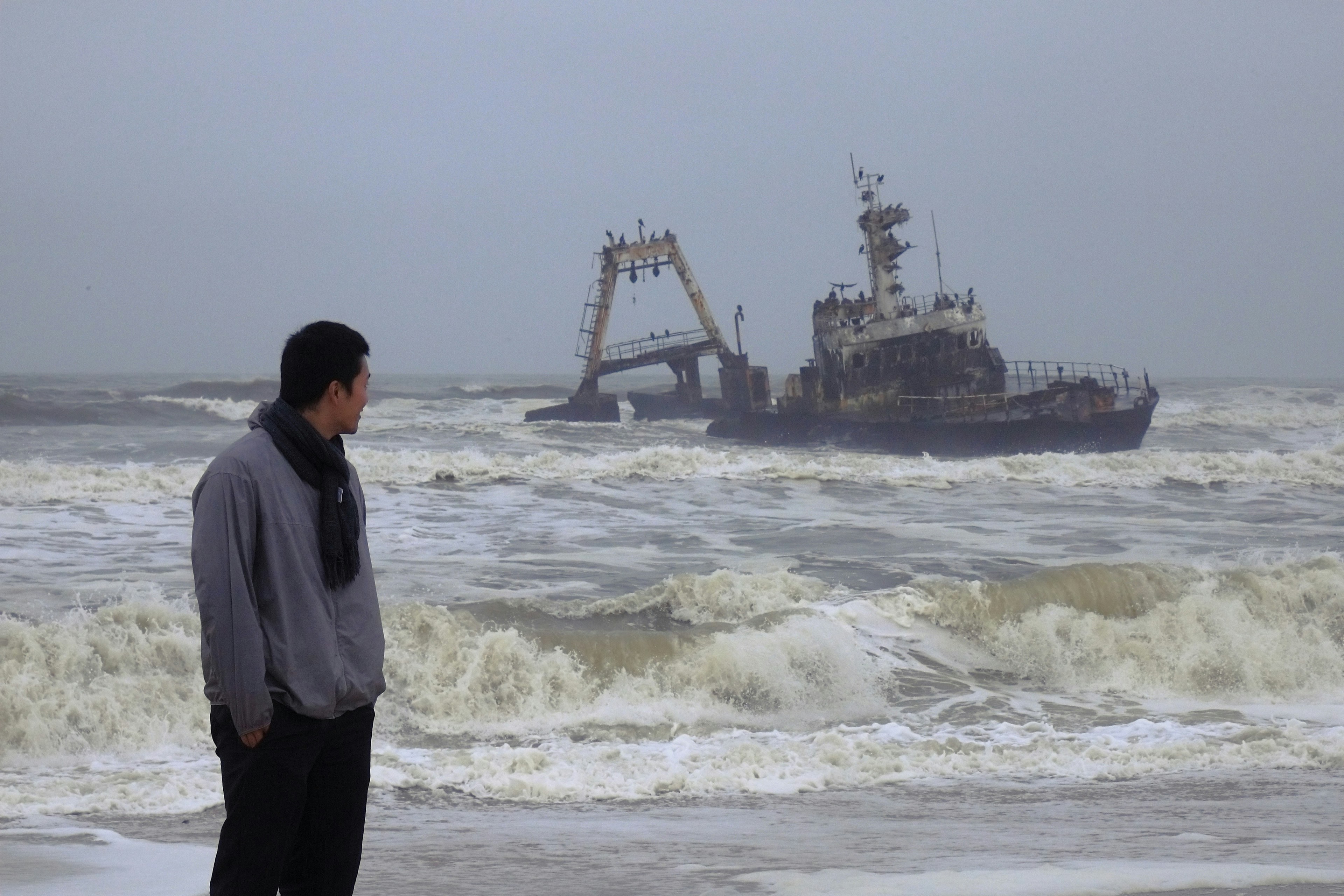 海岸で波を見つめる男性と遠くにある船