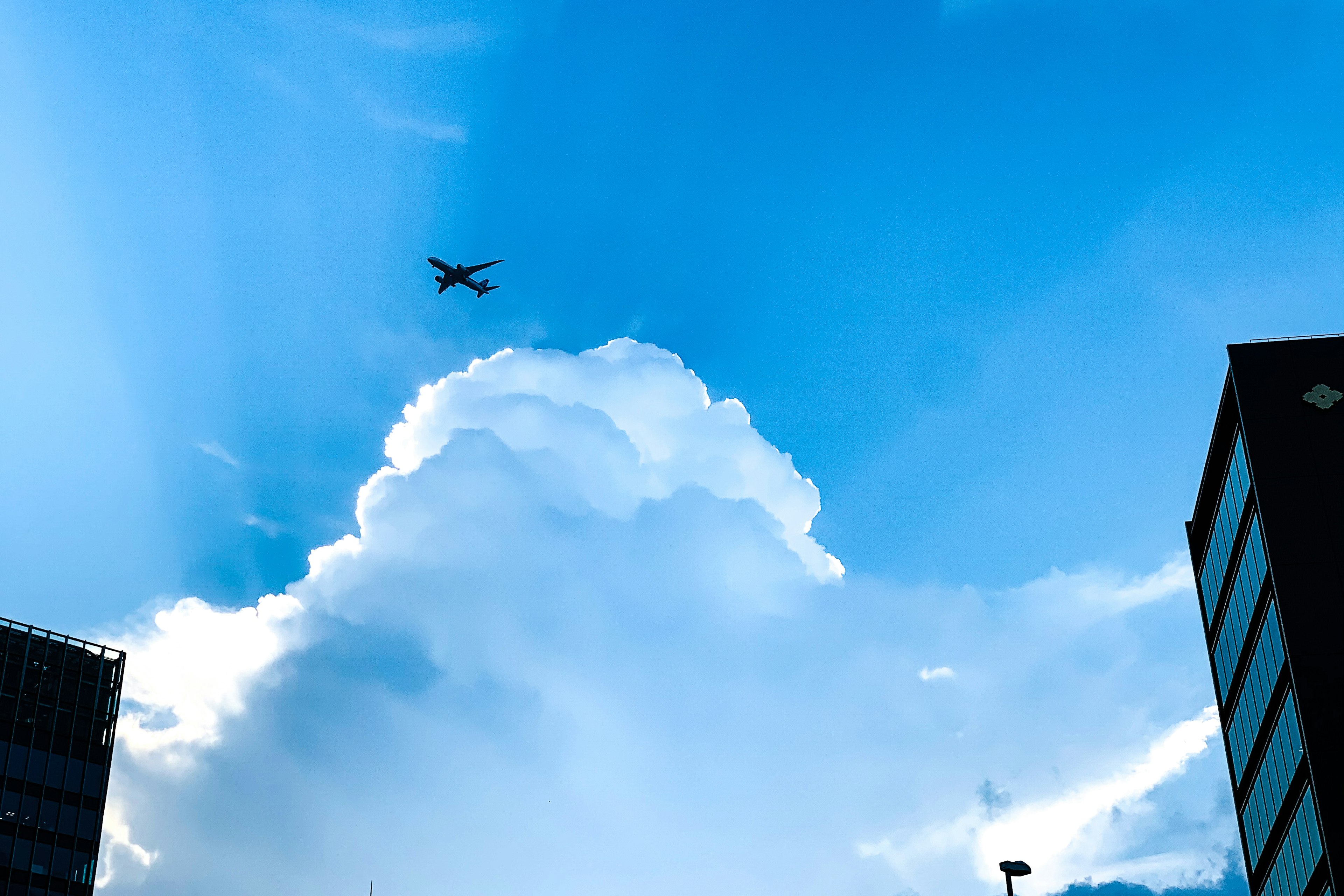 青空に浮かぶ大きな雲と飛行機のシルエット