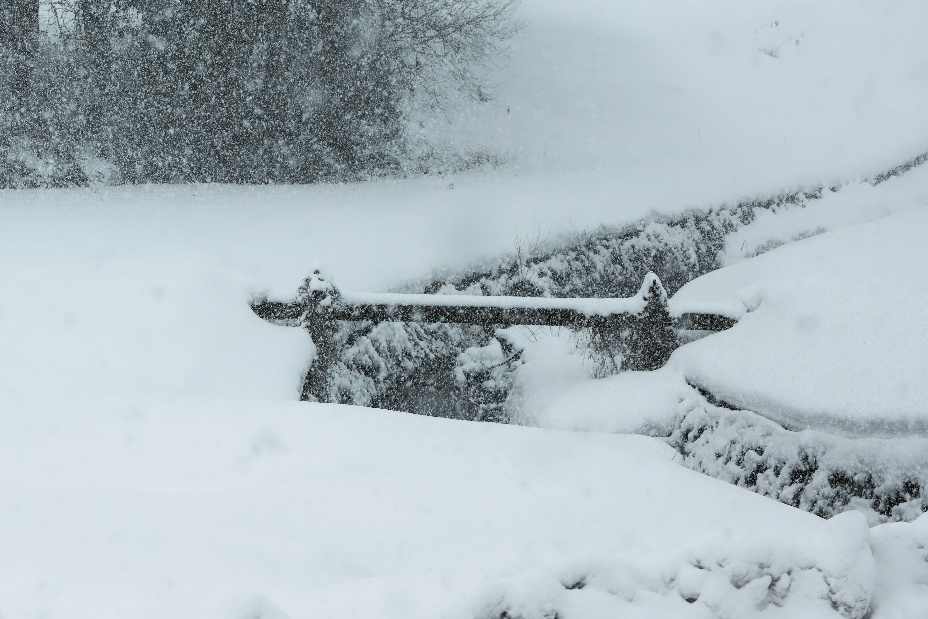 Snow-covered landscape featuring a wooden fence partially buried in snow