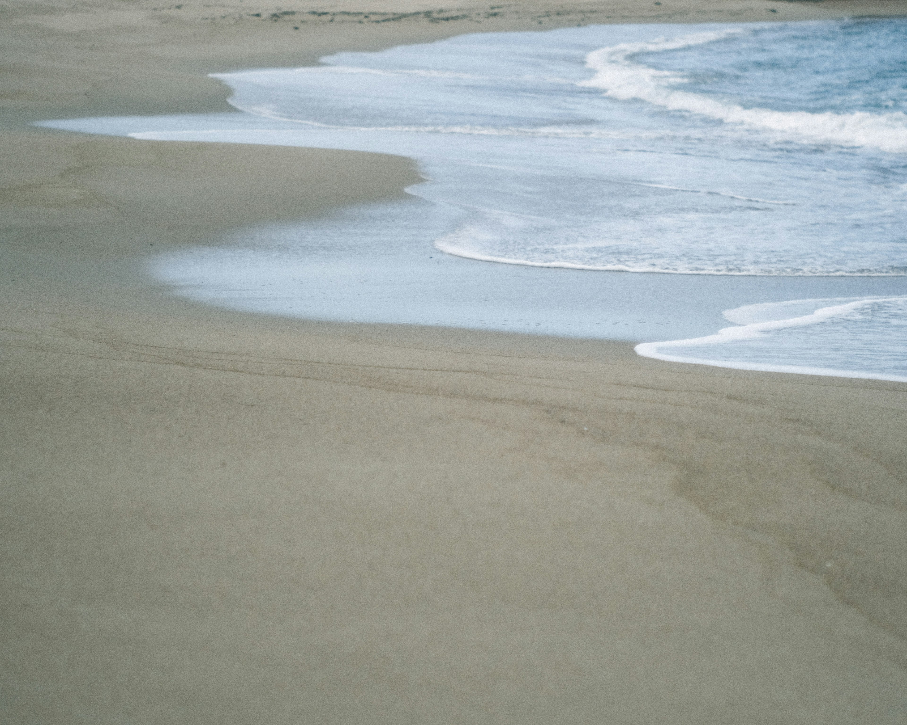 Garis pantai tenang dengan ombak lembut yang menyapu pasir