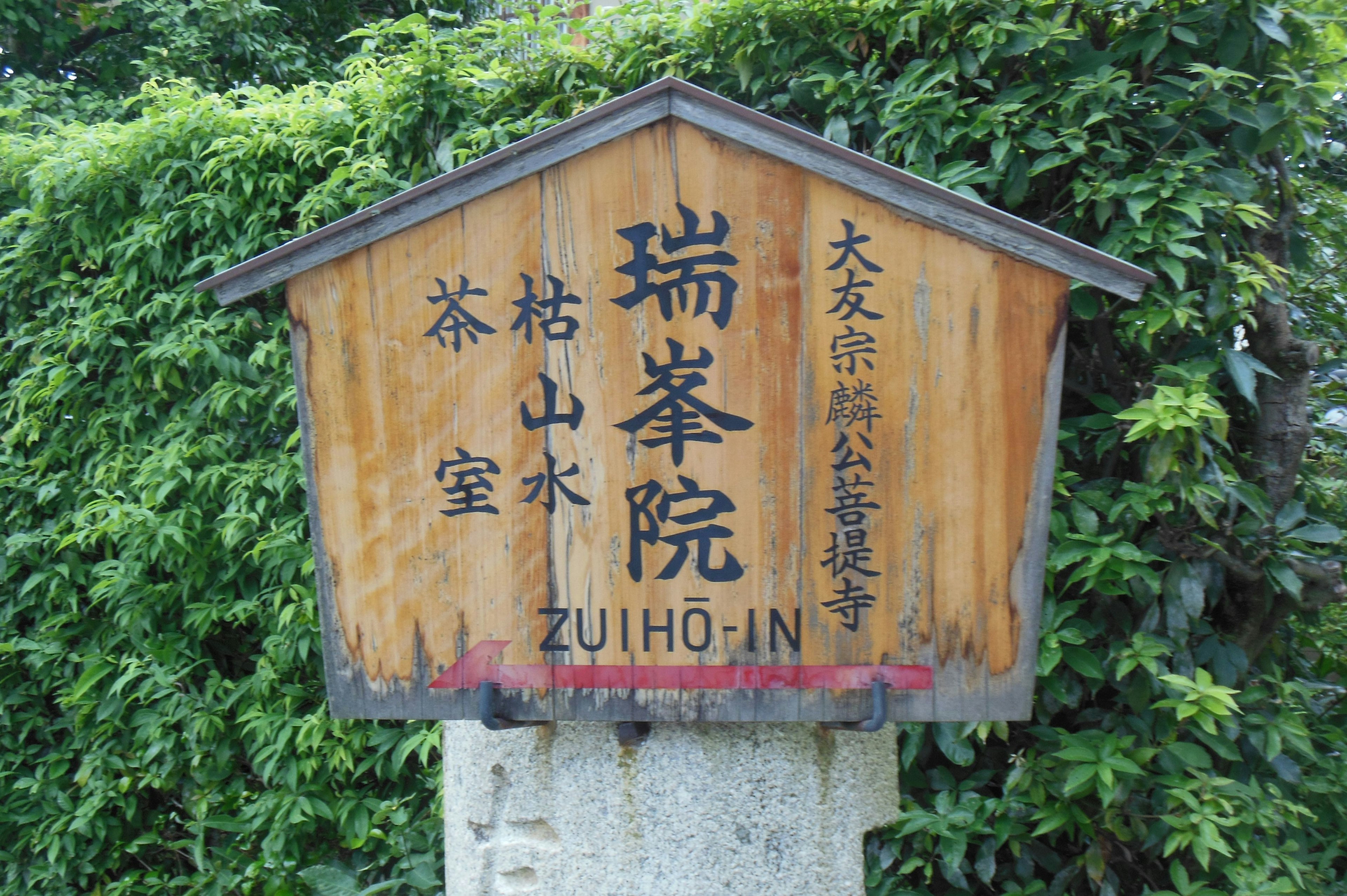 Cartel de madera de ZULHO-IN rodeado de vegetación templo japonés