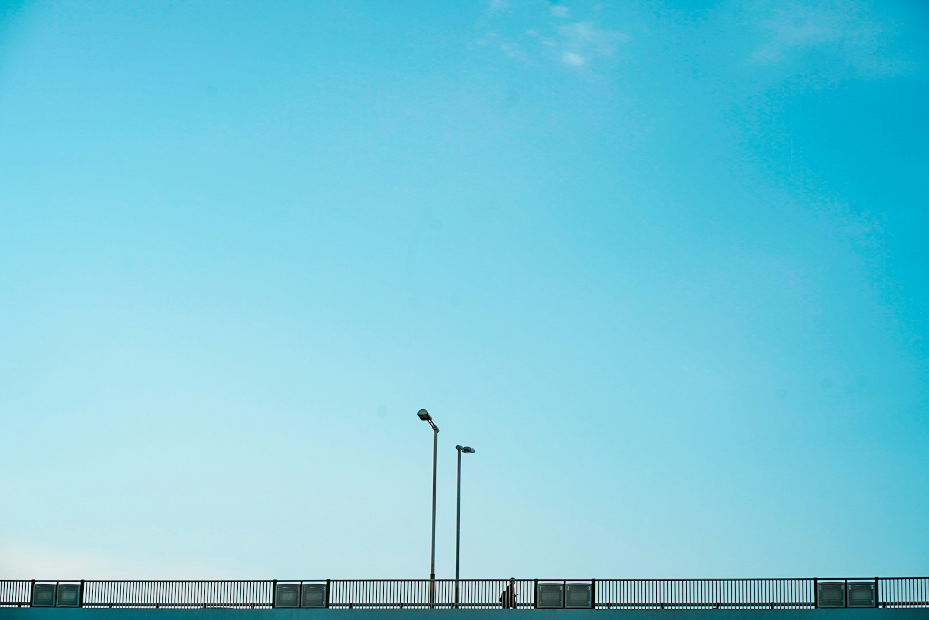 Eine Landschaft mit Straßenlaternen und einem Fußgänger unter einem blauen Himmel