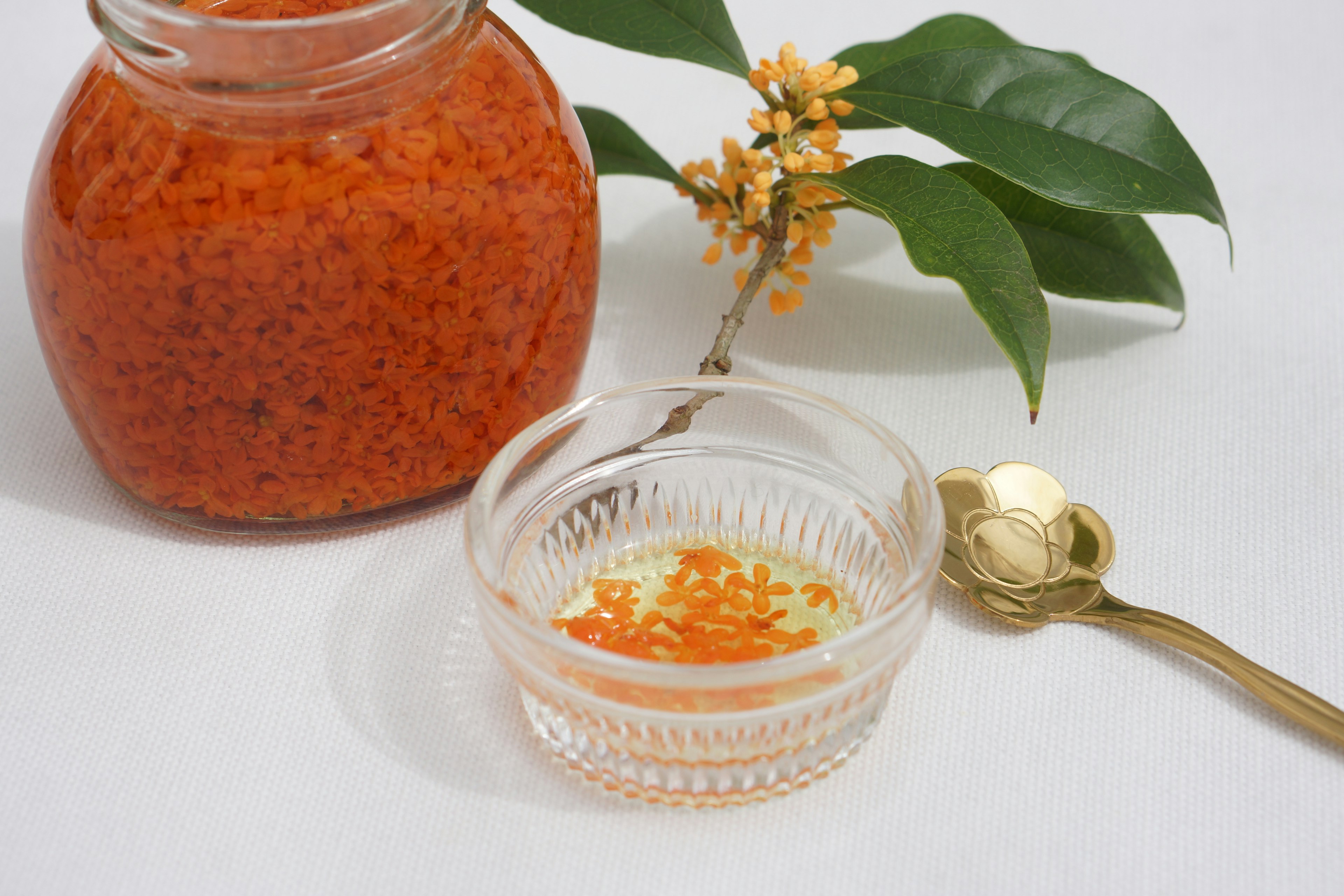 A jar of vibrant orange seasoning next to a small dish with some seasoning and a decorative leaf and flower