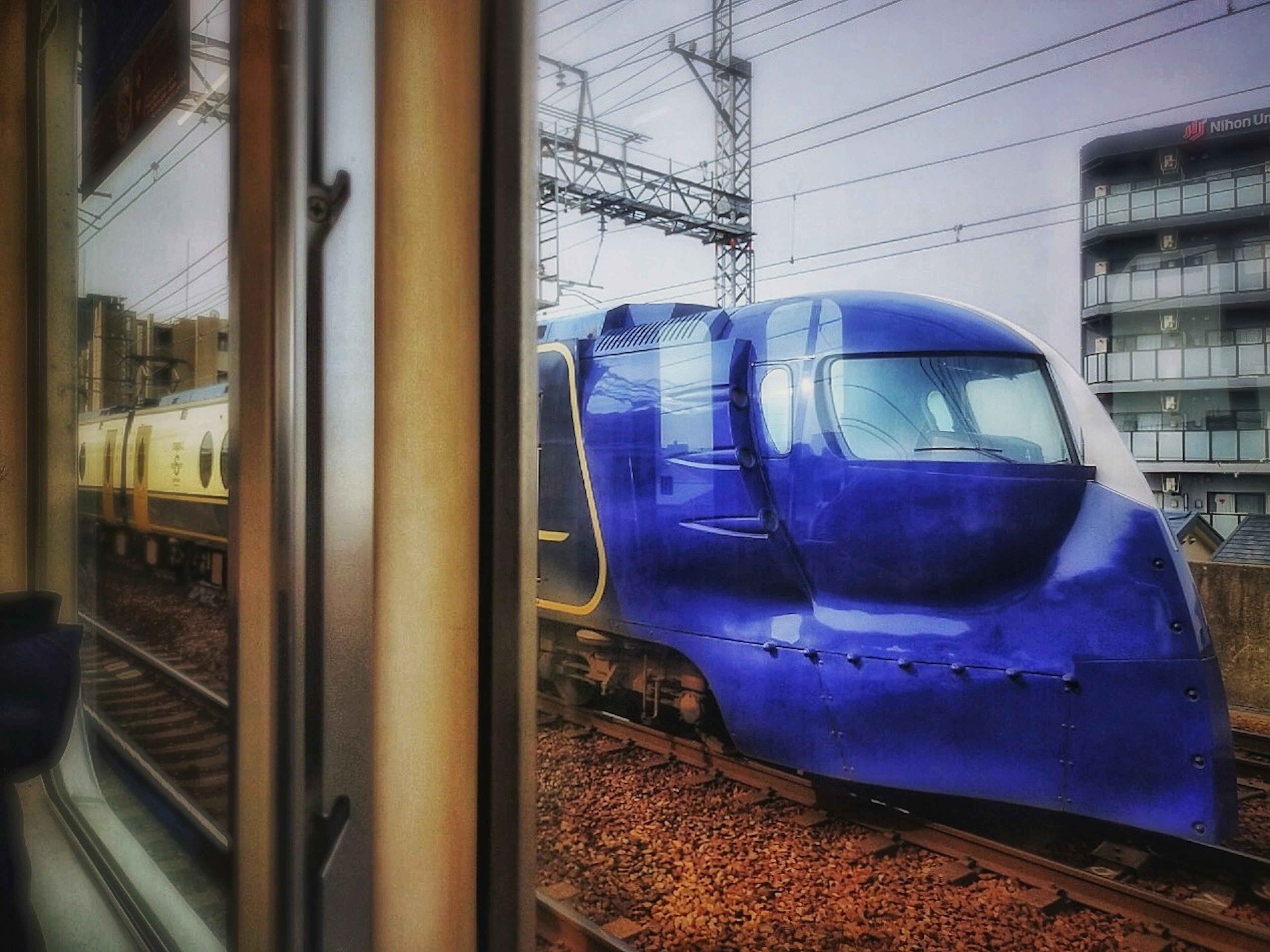 A blue train parked beside the tracks with buildings in the background