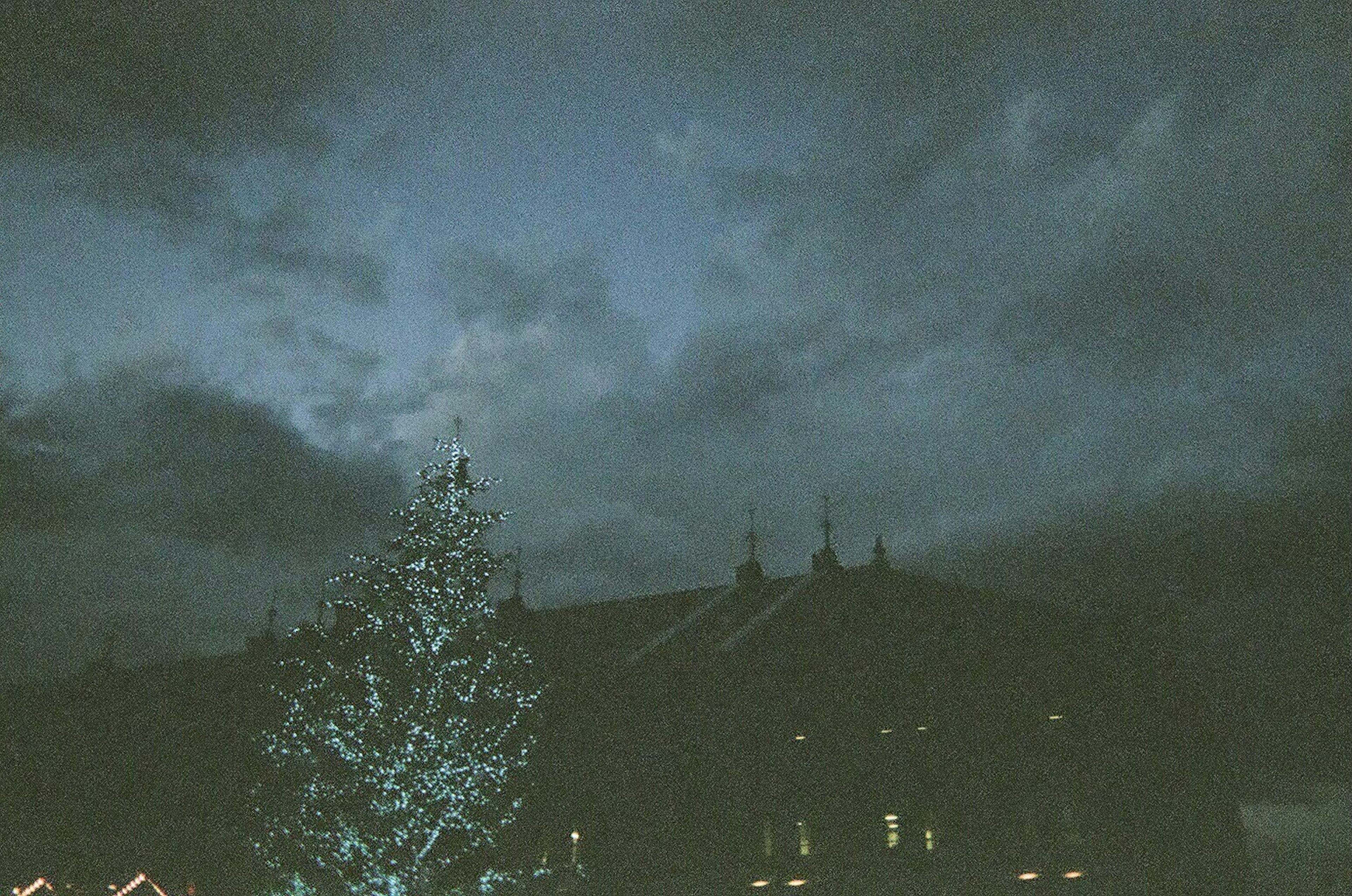 Albero di Natale illuminato in silhouette contro un cielo scuro e edifici