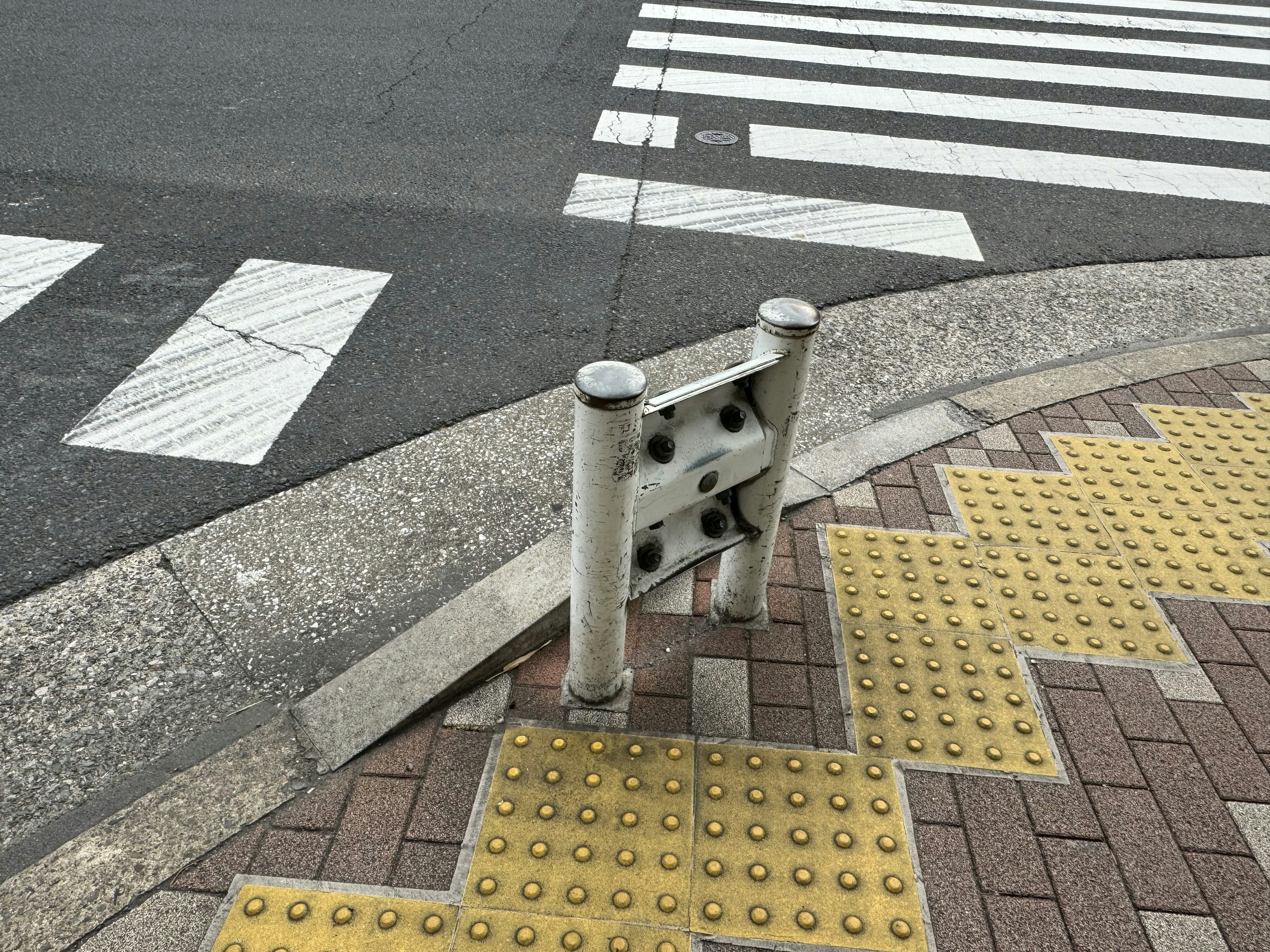 Penghalang logam putih di zebra cross dengan ubin taktil kuning