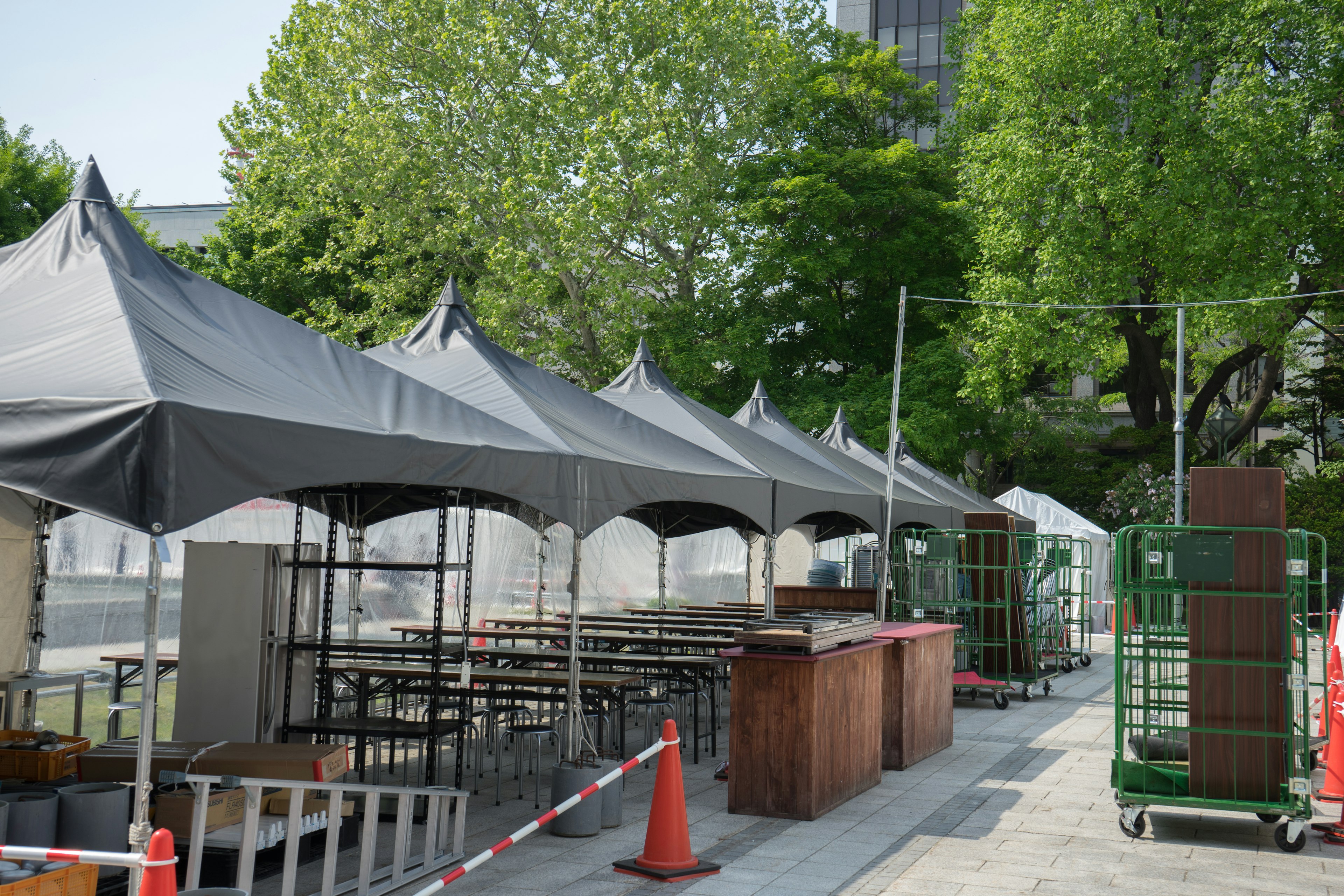 Scène extérieure avec des rangées de tentes et de tables entourées de verdure