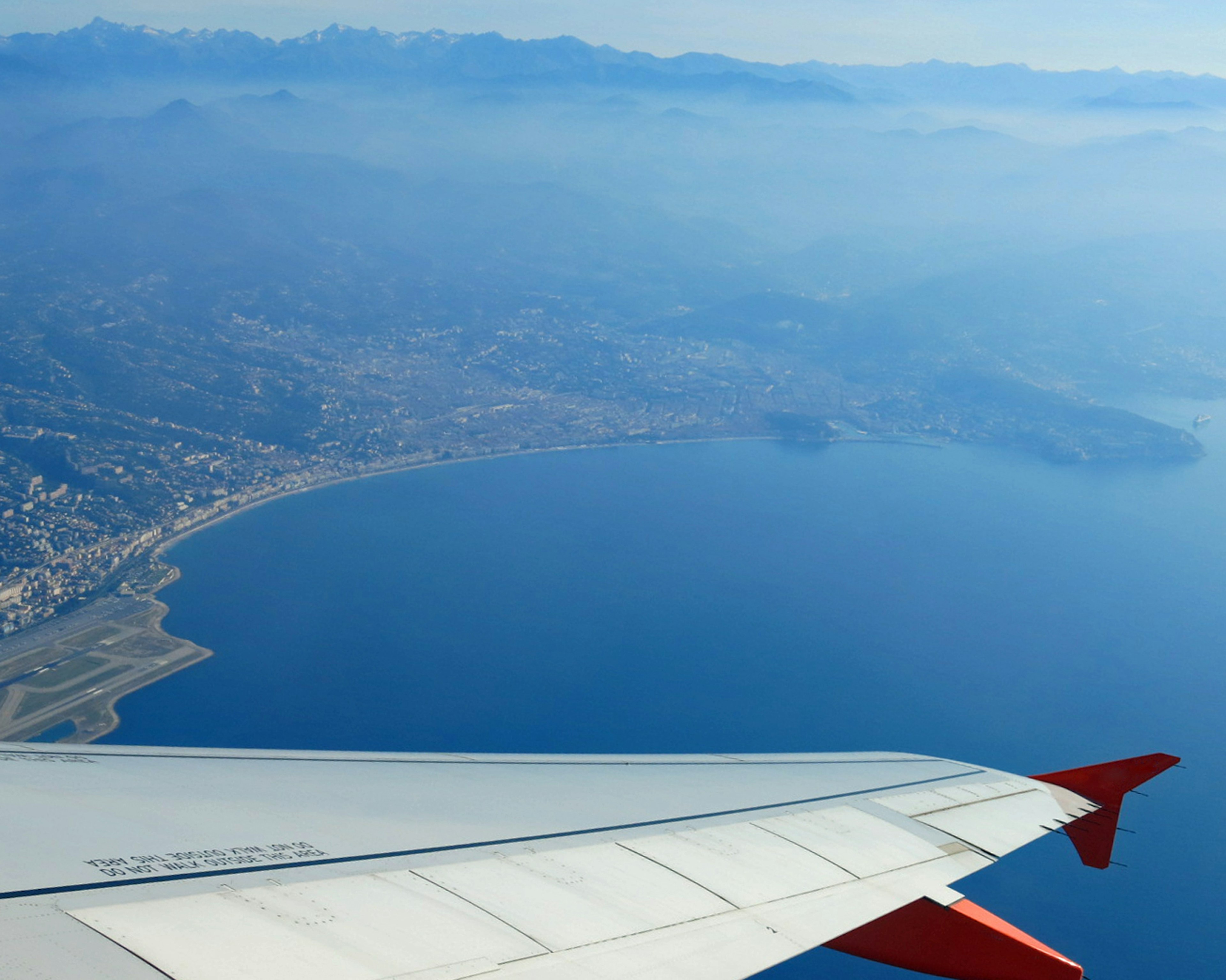 Aerial view of coastline and mountains airplane wing in frame