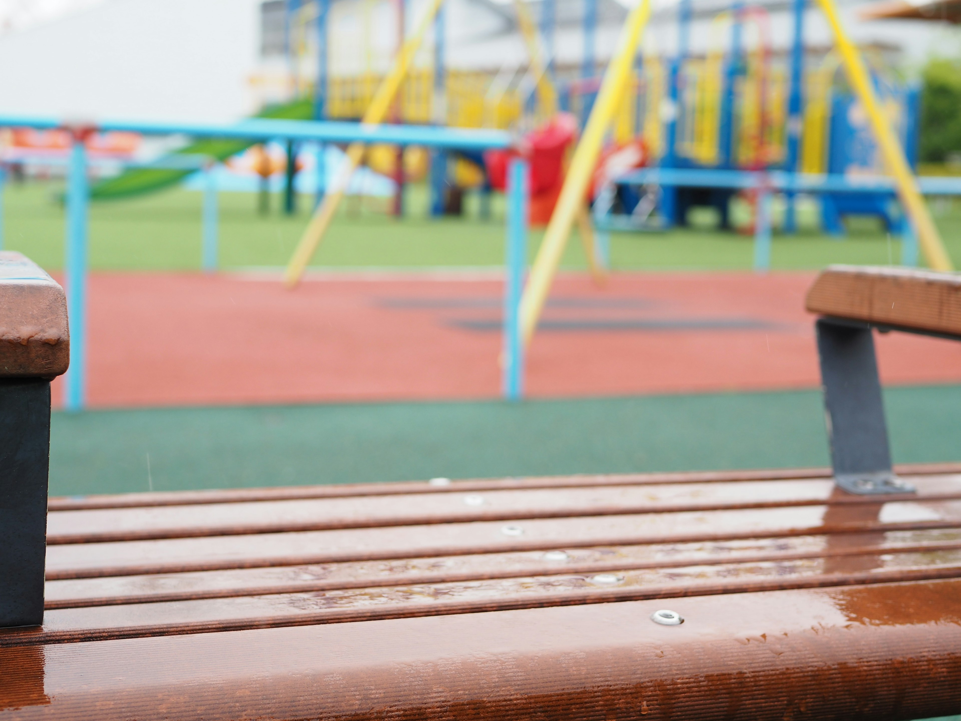 Nahaufnahme einer Parkbank mit Spielgeräten im Hintergrund