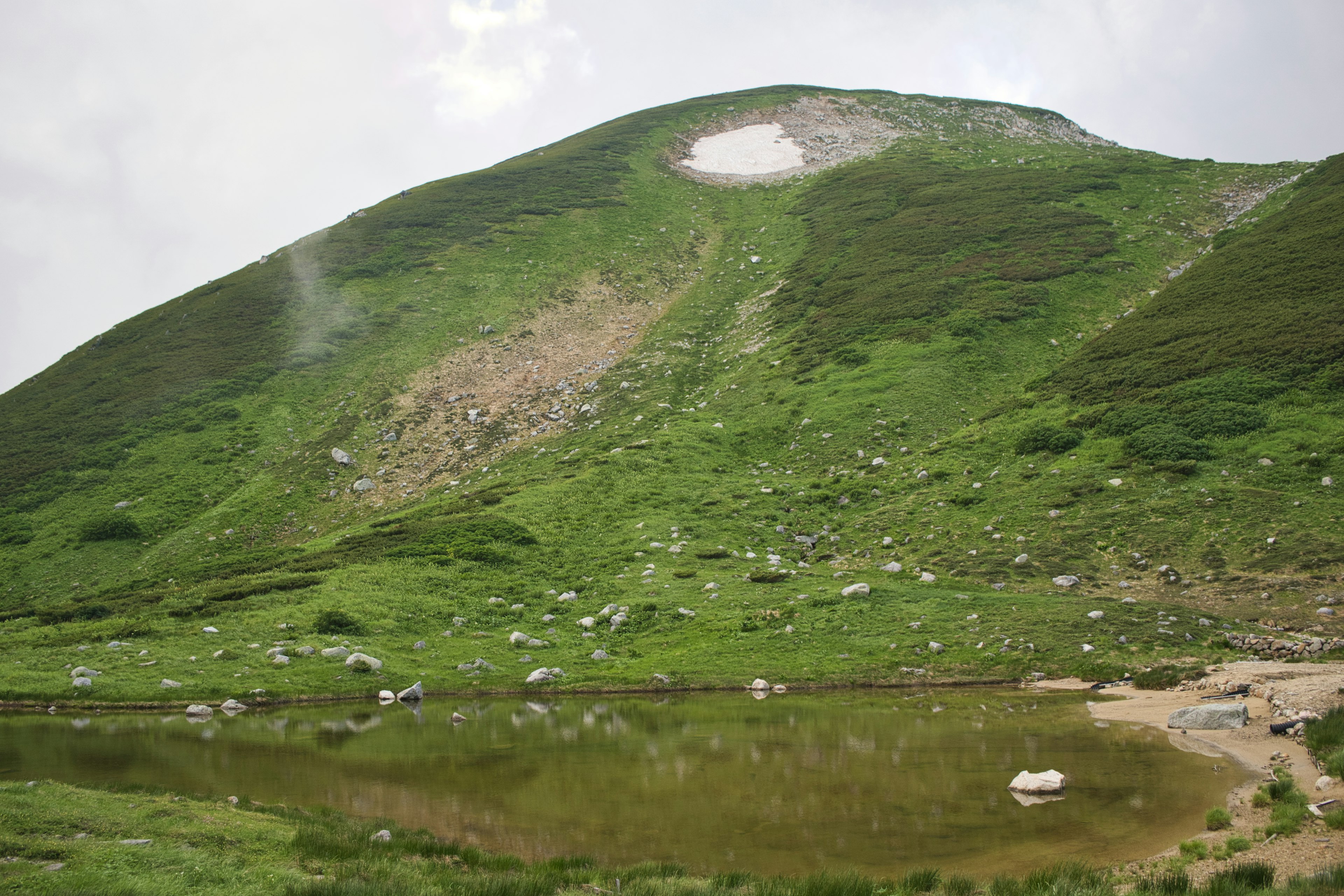 Mountain slope covered in green grass with a small pond