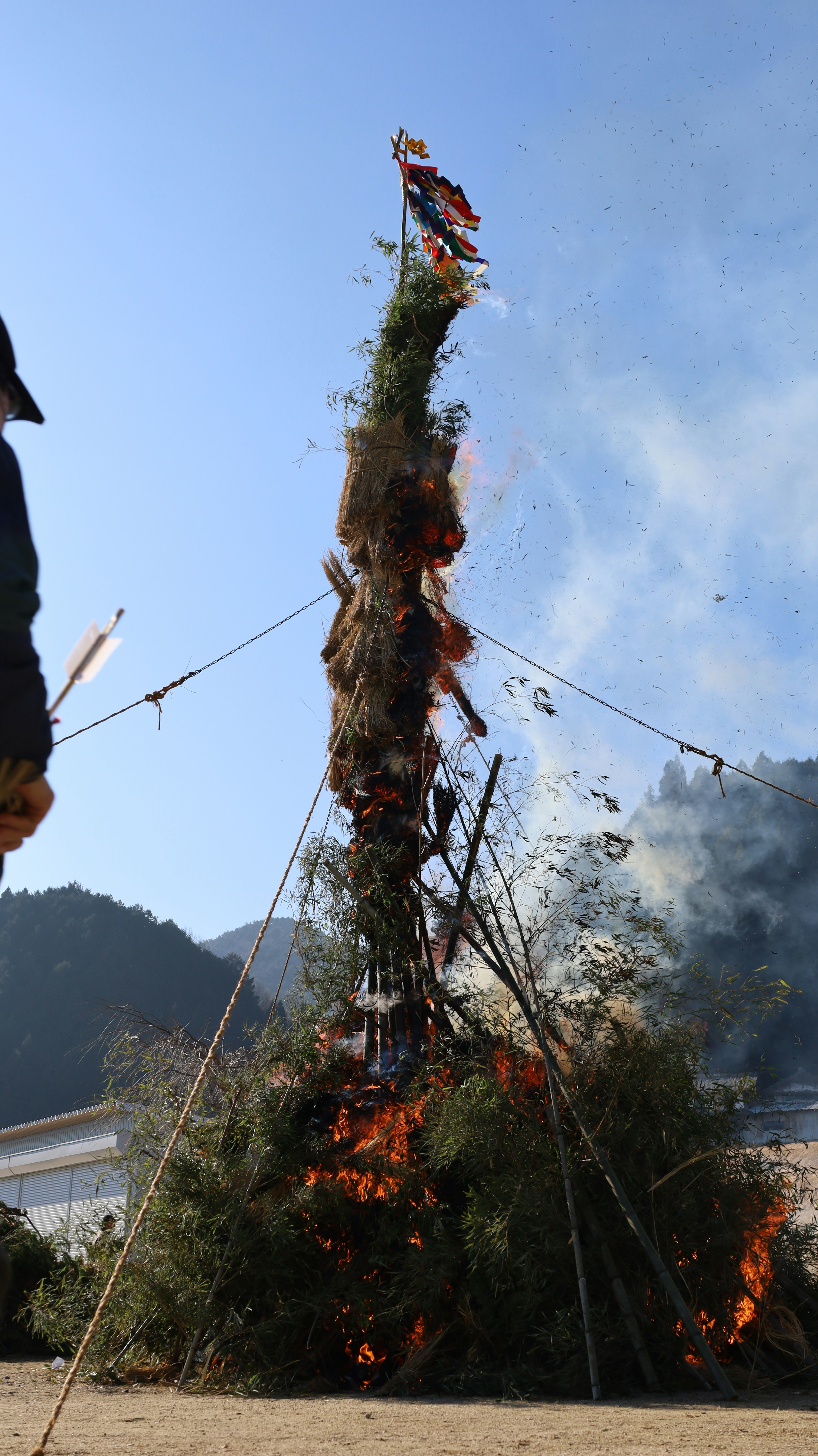 Grande pira con fiamme che si alzano circondata da un paesaggio naturale