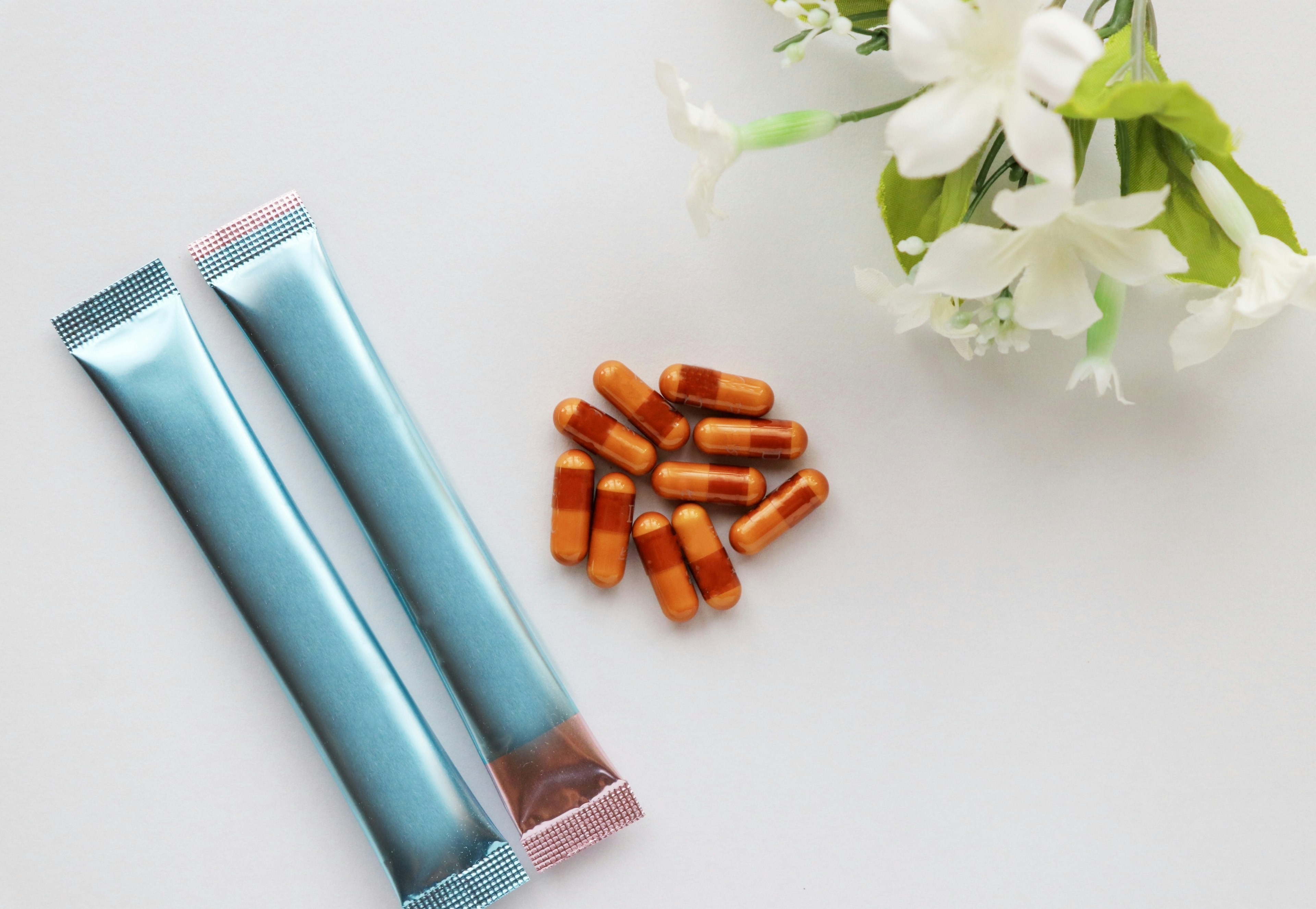 Still life featuring blue packaging and orange capsules with white flowers