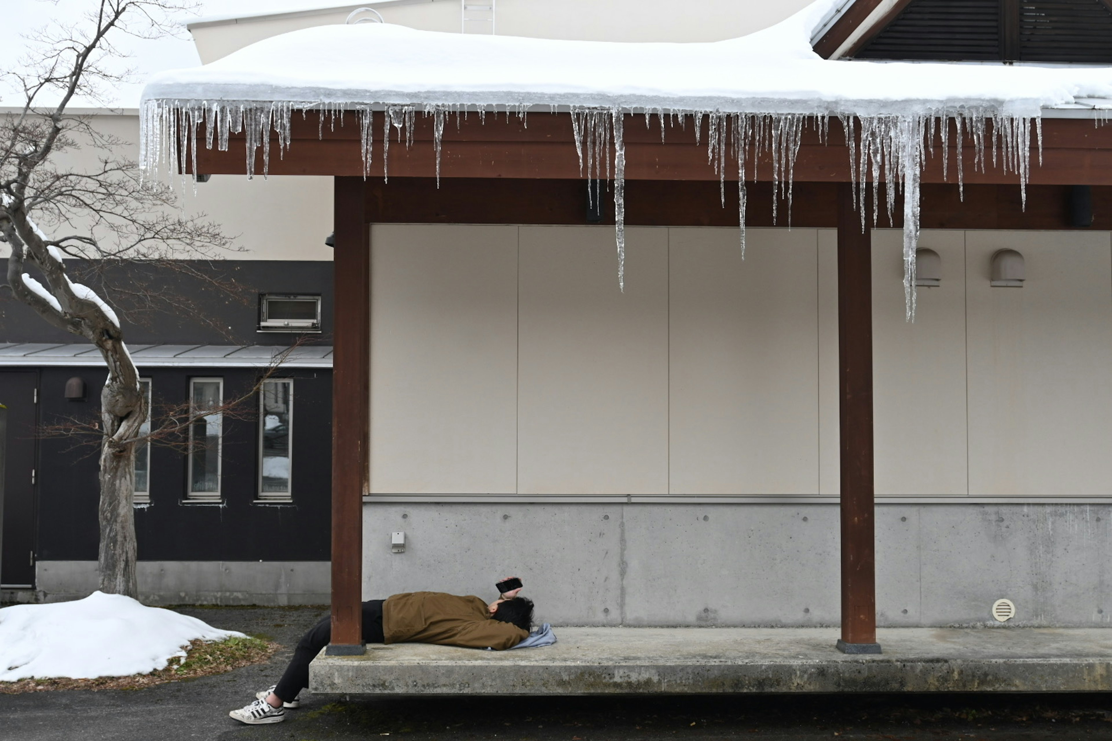 躺在雪上的人和屋頂懸掛的冰柱