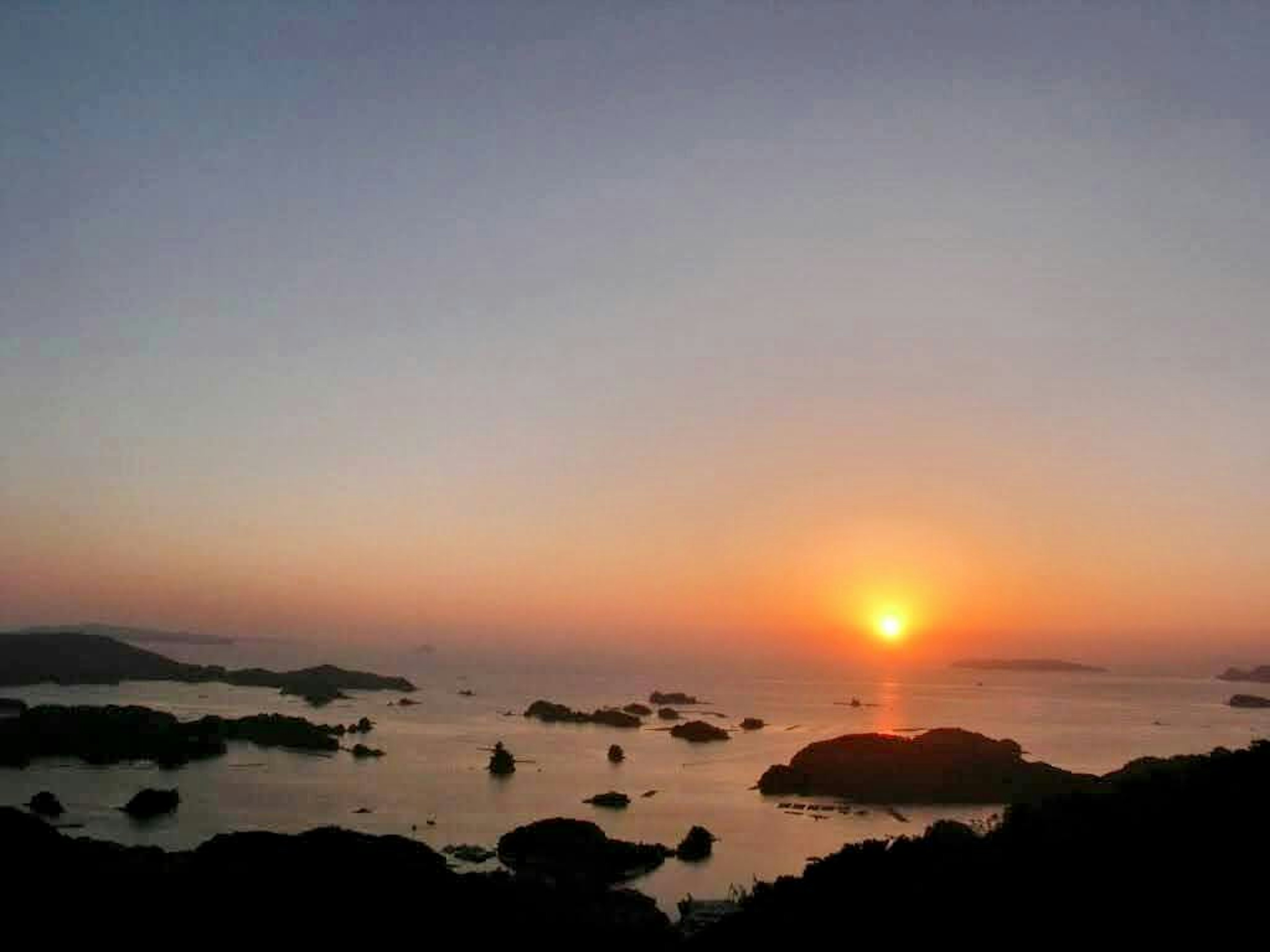 Beautiful sunset over the ocean with scattered rocks reflecting orange sun on the water