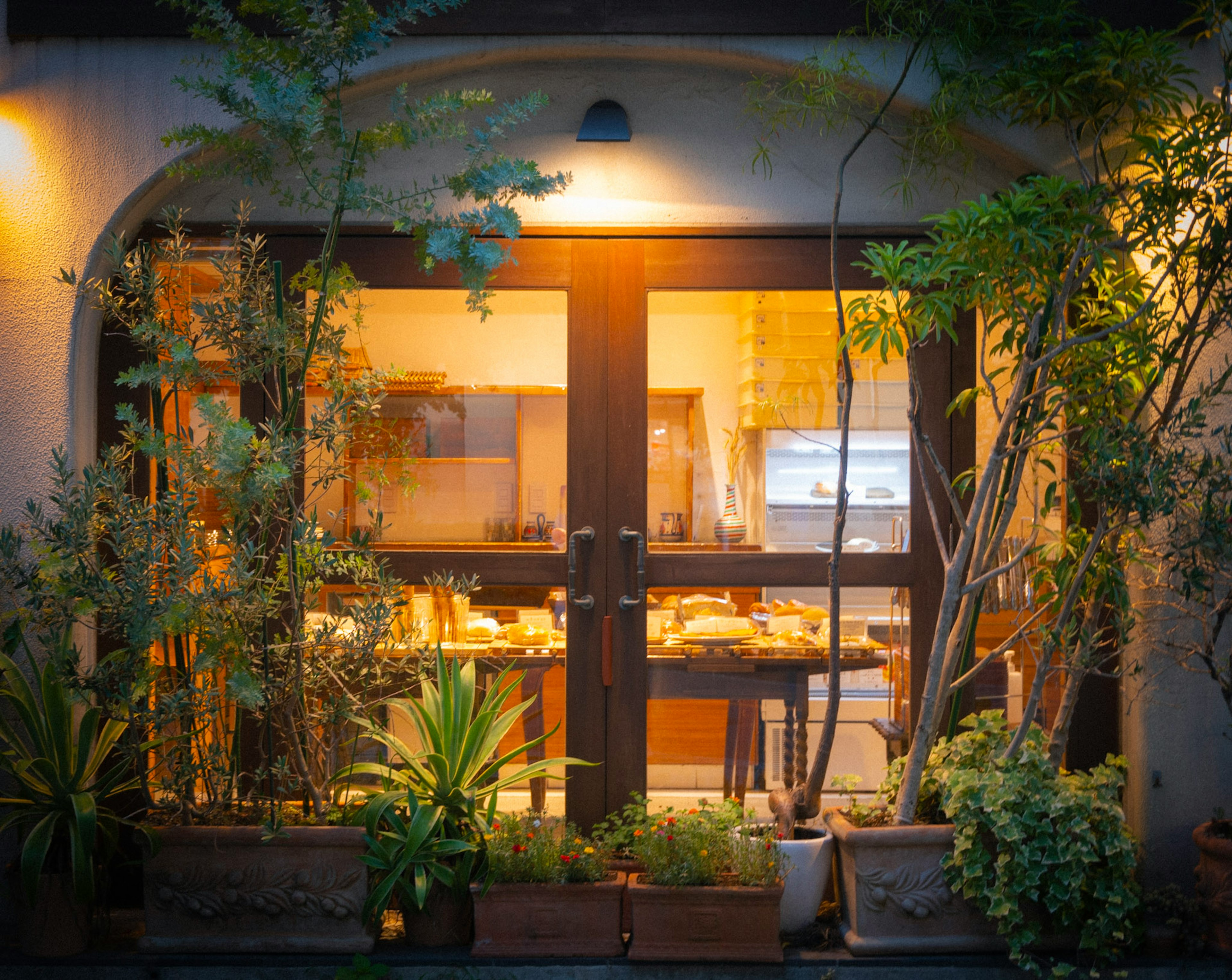 Exterior de una cafetería con luz cálida que brilla a través de las ventanas rodeada de vegetación