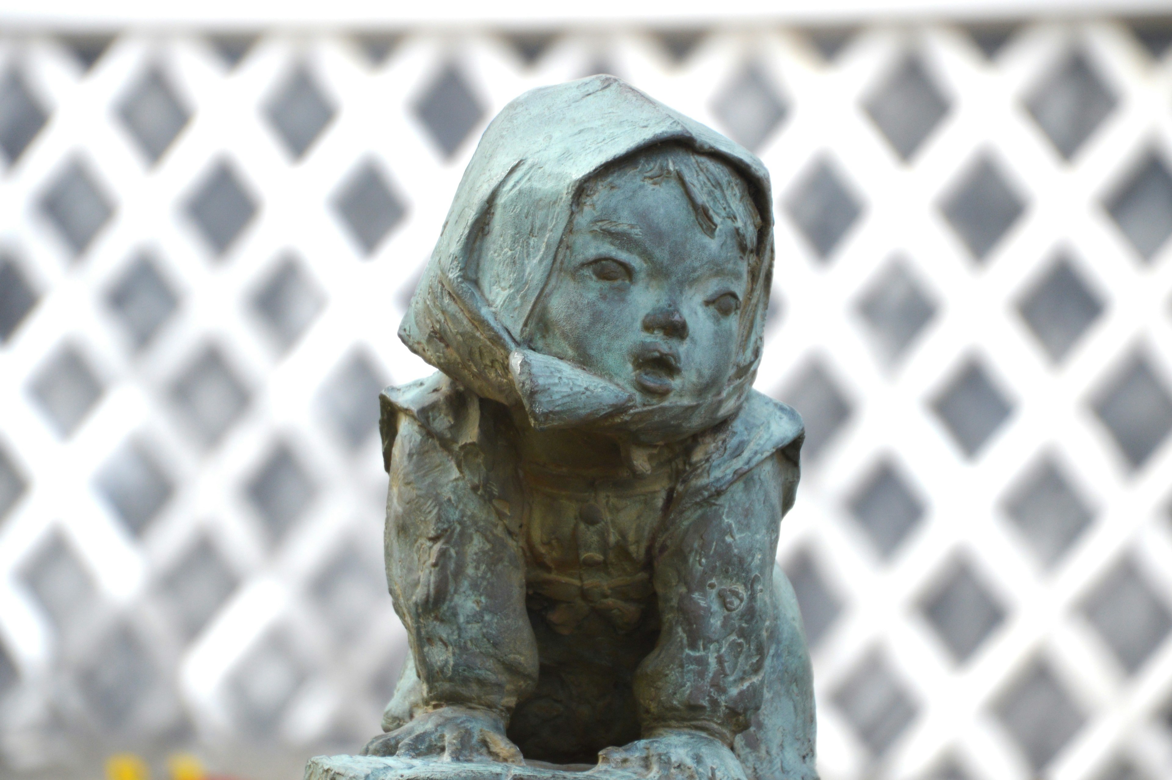 Bronze statue of a child in the foreground with a white lattice background