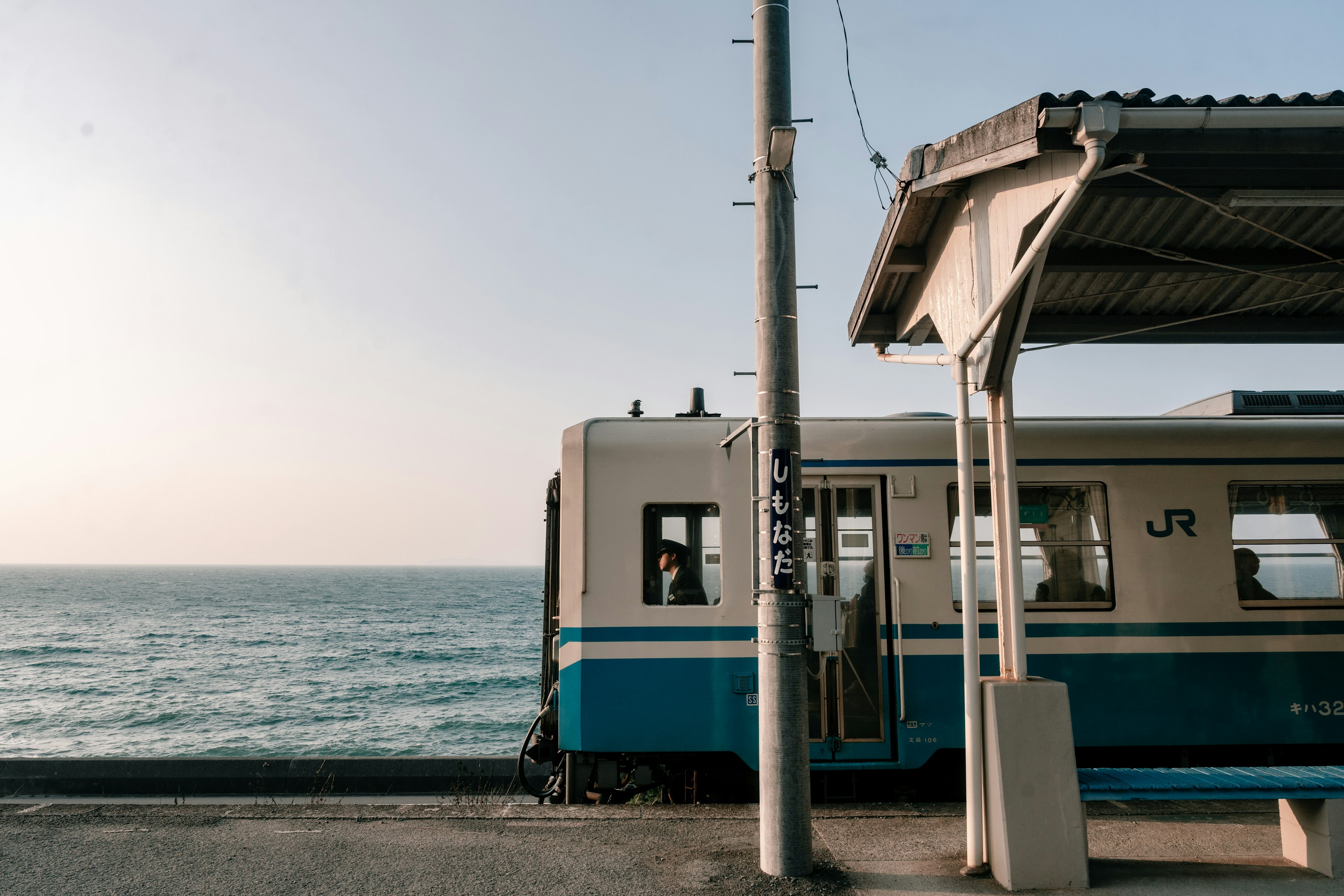 Blue JR train parked near the ocean with a train station