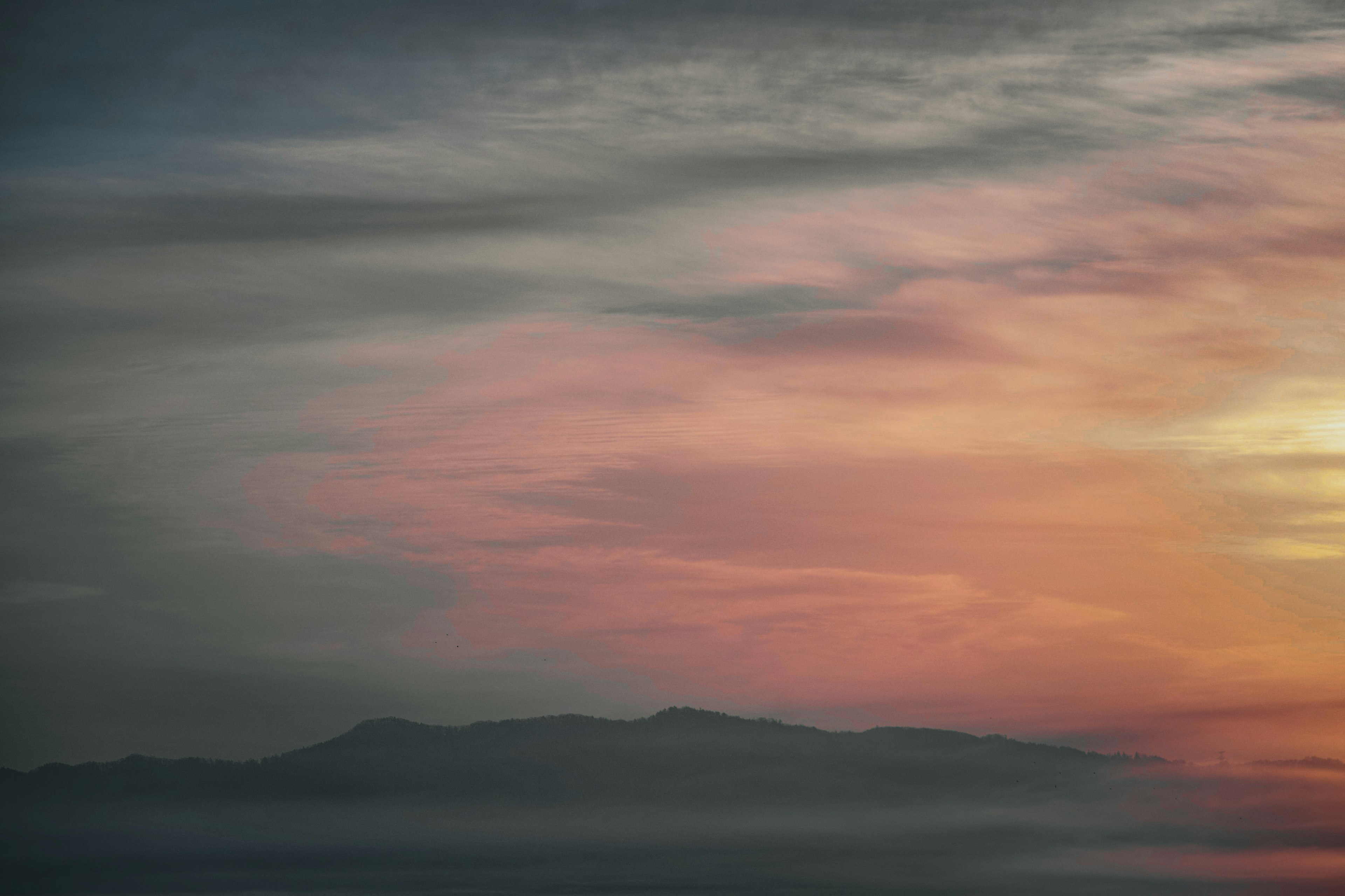 Silhouette of a mountain against a moody sky with orange sunset hues