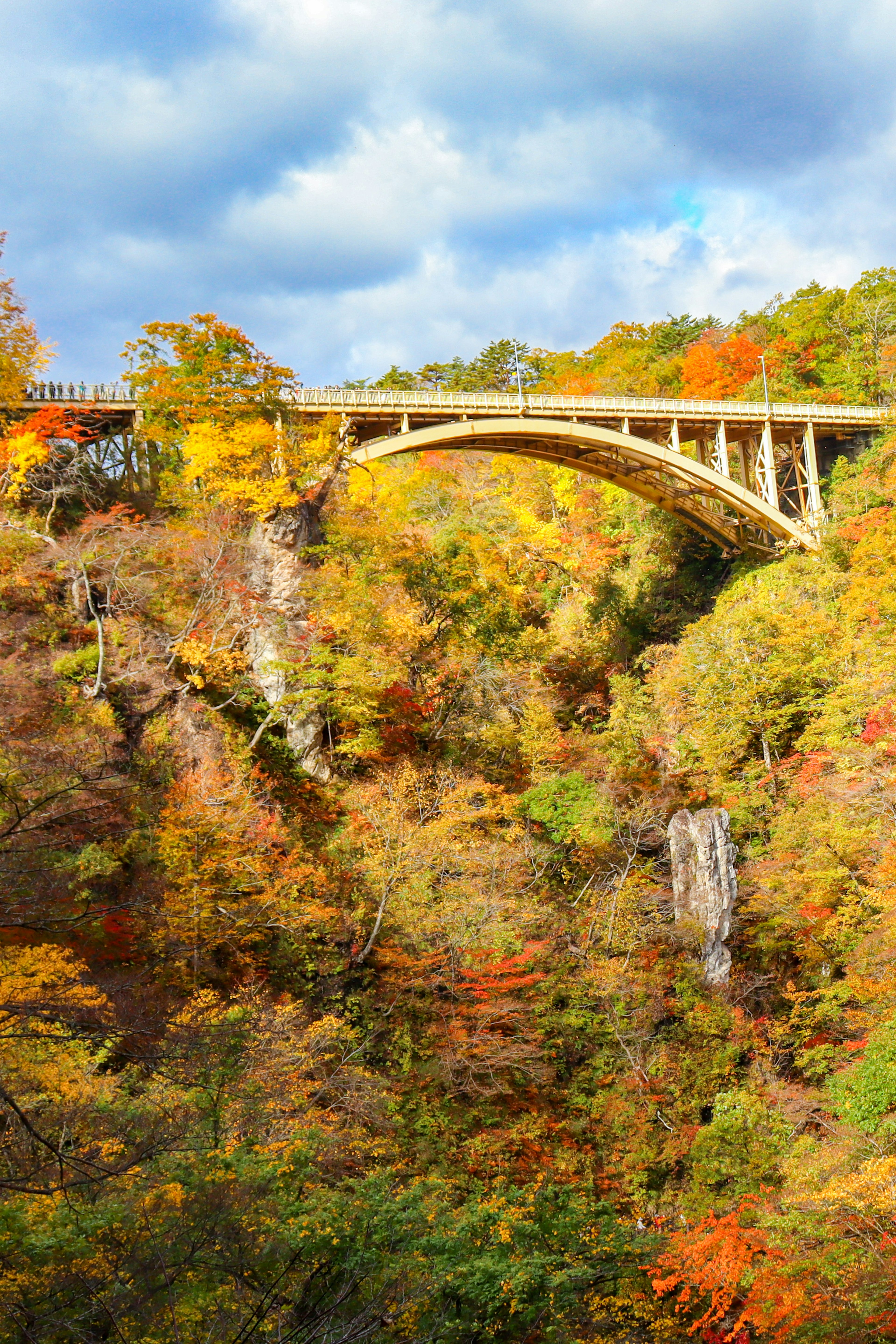 A scenic view of a bridge and waterfall surrounded by autumn foliage